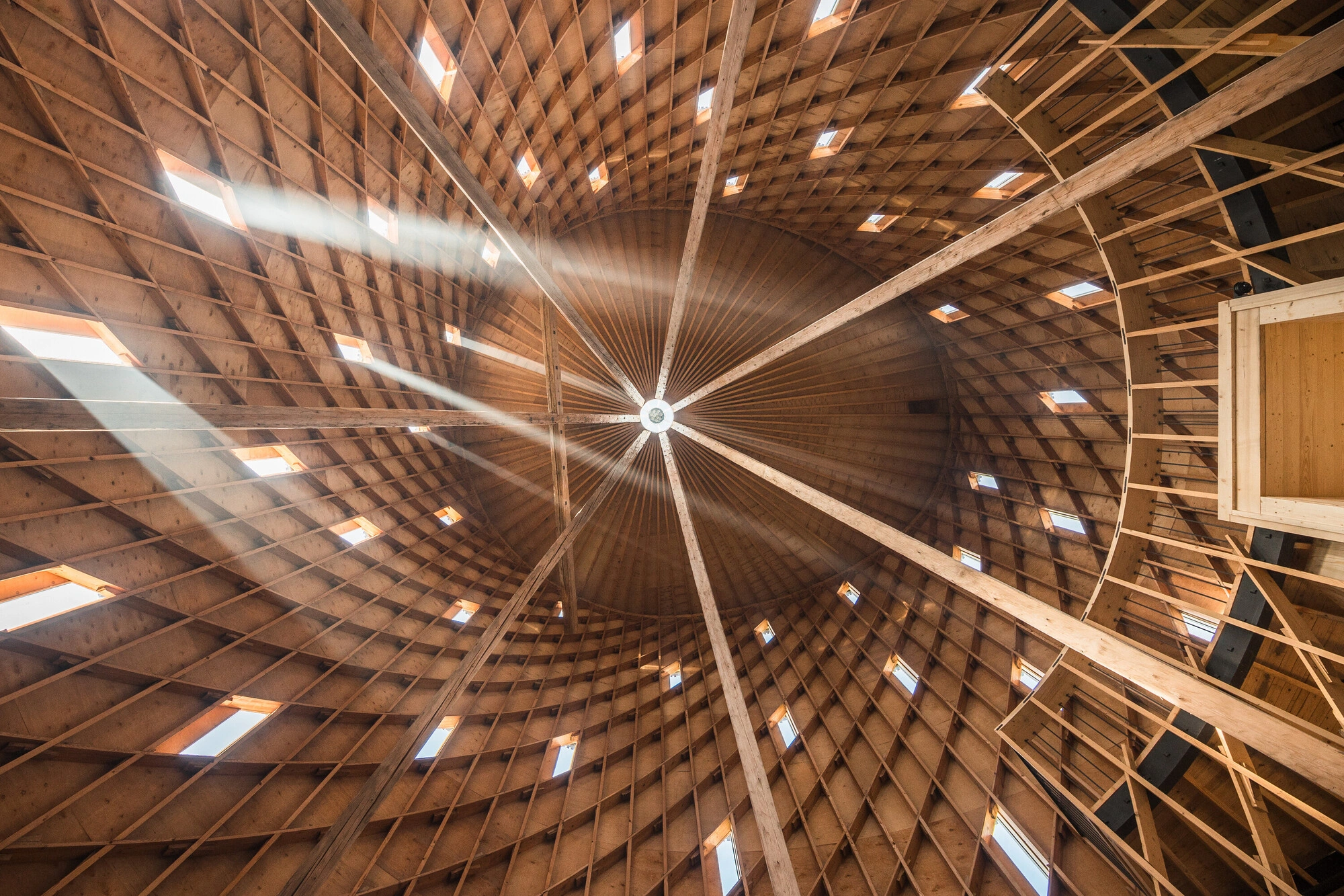Our Lady of Sorrows Chapel by RCNKSK — Upward view of the chapel's radial timber roof structure, with seven ascending beams converging toward a central circular aperture.