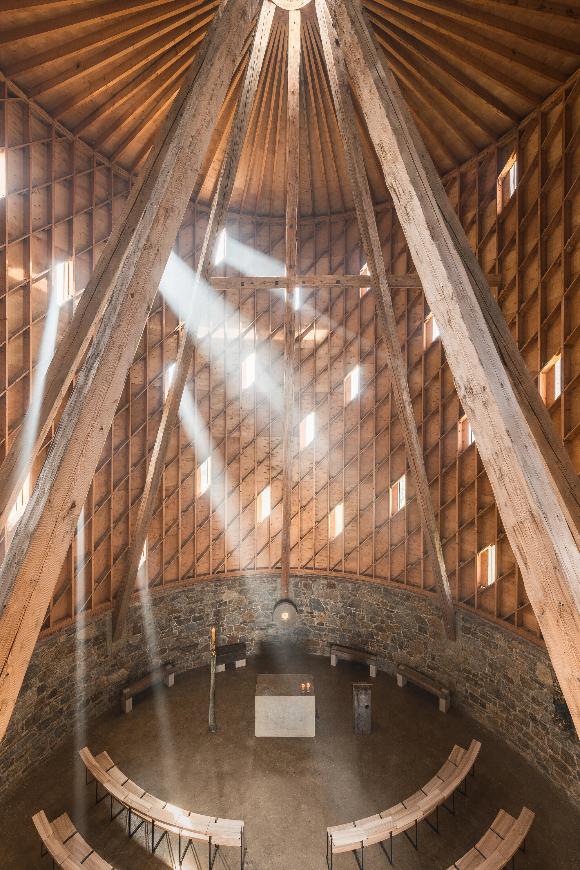 Our Lady of Sorrows Chapel by RCNKSK — Overhead view into the chapel's interior reveals the radial timber roof structure converging toward a central skylight, with seven ascending beams creating...