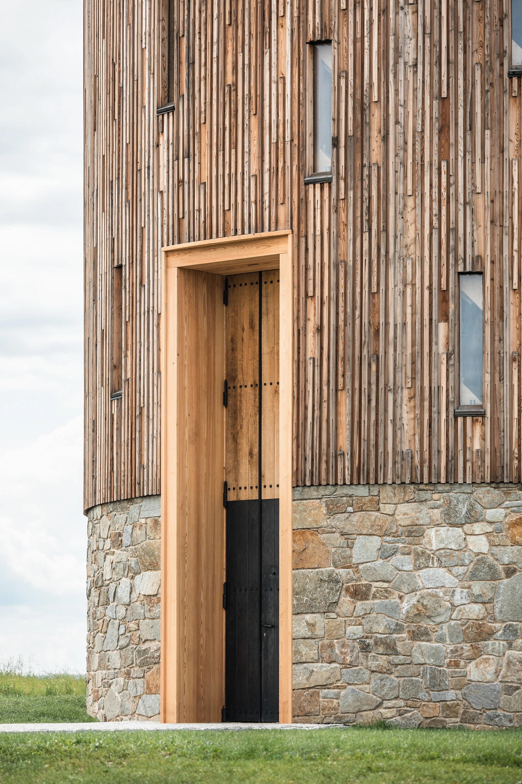 Our Lady of Sorrows Chapel by RCNKSK — The chapel's threshold presents a studied composition of material contrasts: a timber-framed doorway with natural wood tones set within a stone-faced base...