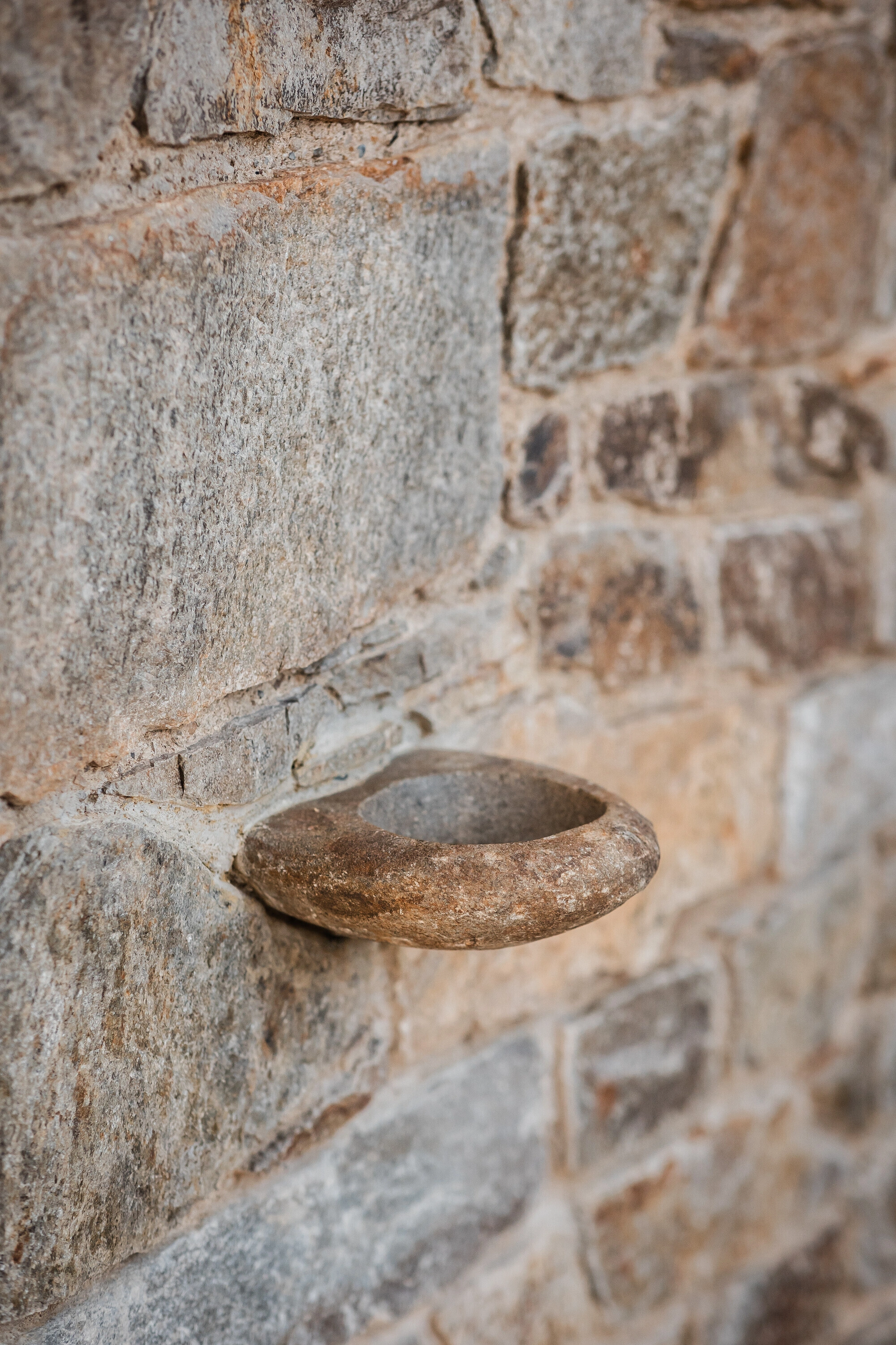 Our Lady of Sorrows Chapel by RCNKSK — A close-up detail of the chapel's masonry wall reveals a weathered stone surface with horizontal mortar joints and a bronze or brass handle—likely...