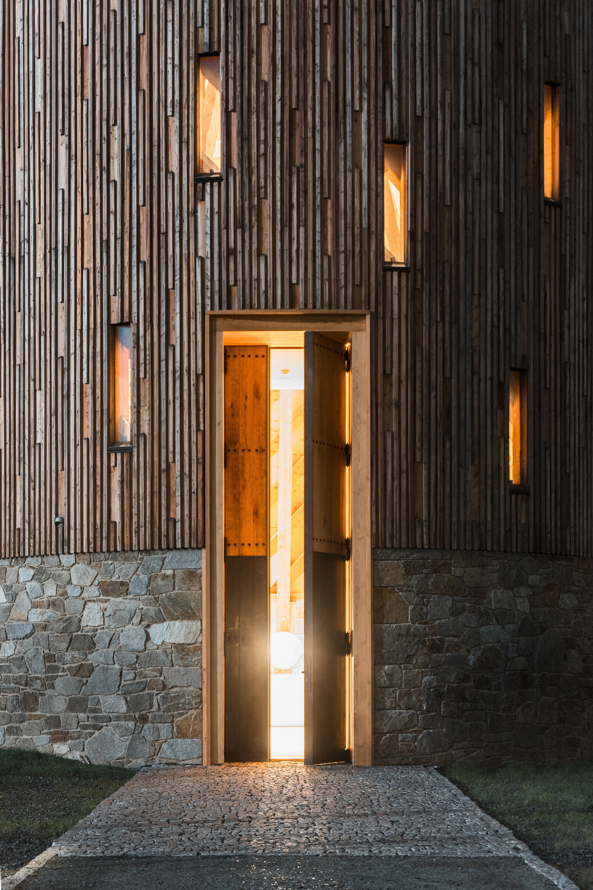 Our Lady of Sorrows Chapel by RCNKSK — Night-time photograph of the chapel entrance captured with the wooden double doors open, revealing warm interior lighting.