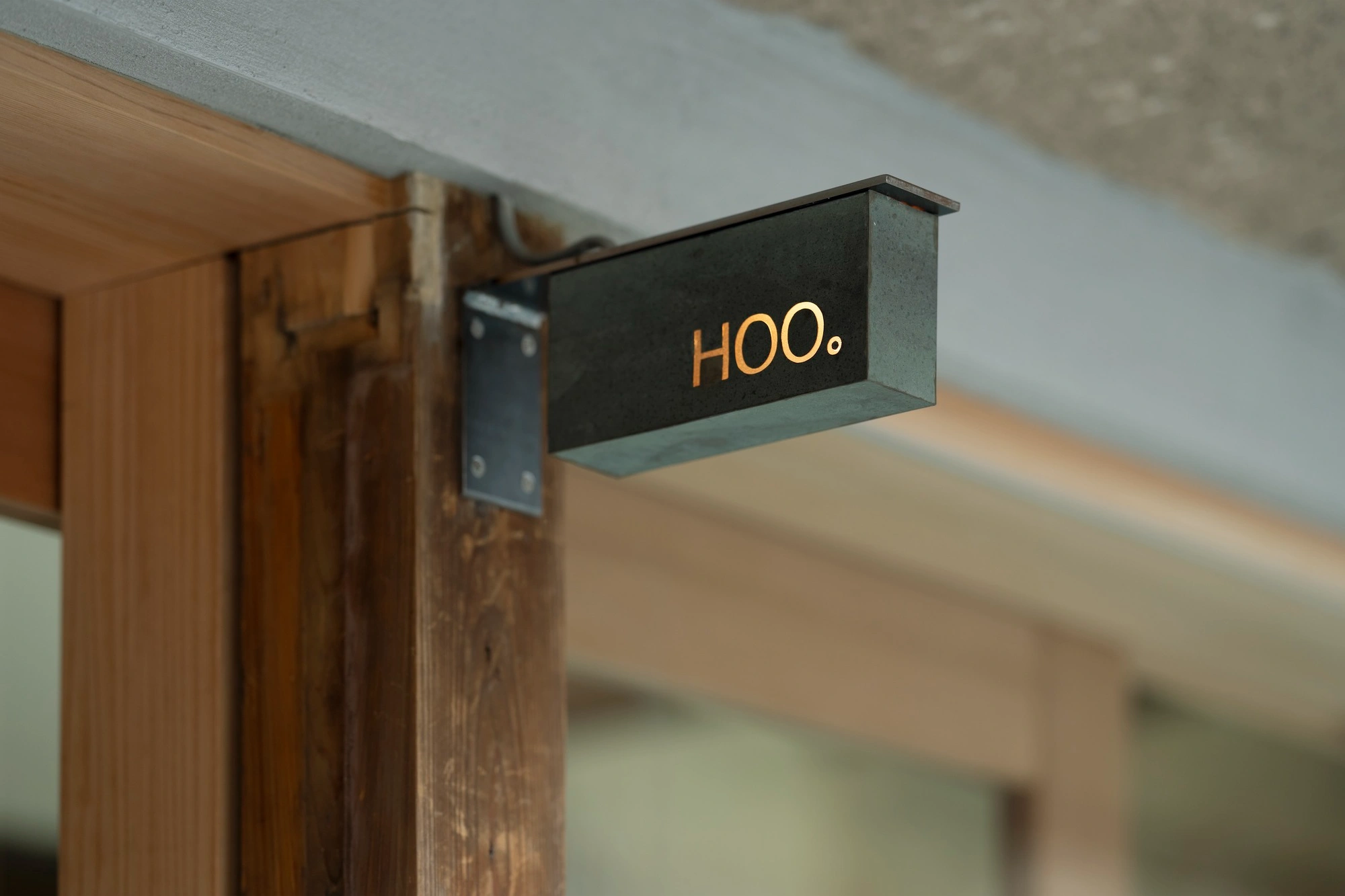 HOO Cafe Kyoto by Koyori Architects — A dark patinated metal signage box extends horizontally from the timber-framed storefront, displaying 'HOO.' in warm brass lettering.