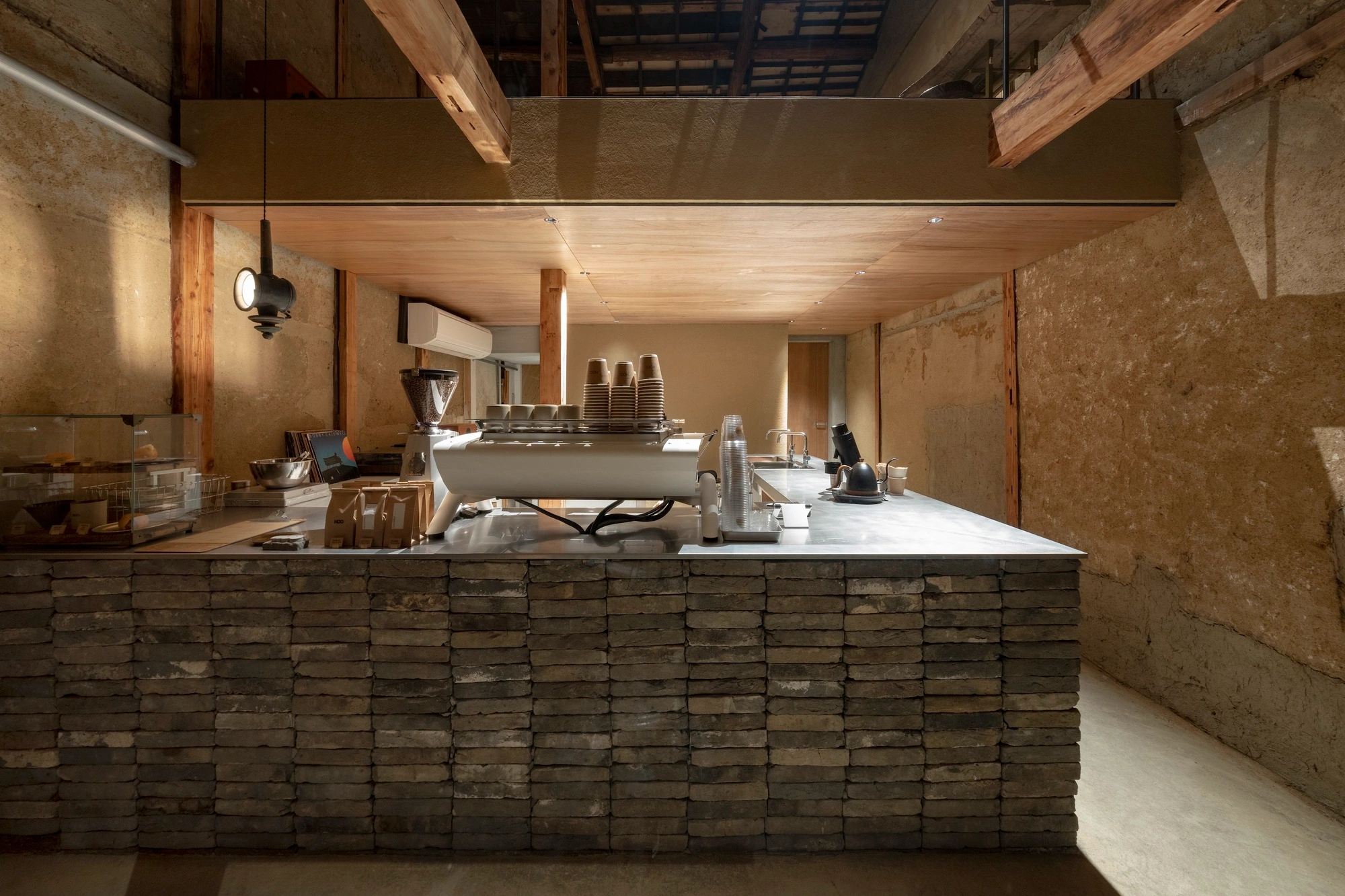 HOO Cafe Kyoto by Koyori Architects — Interior view of HOO Cafe's service counter, where rendered concrete walls with visible weathering establish the spatial envelope.