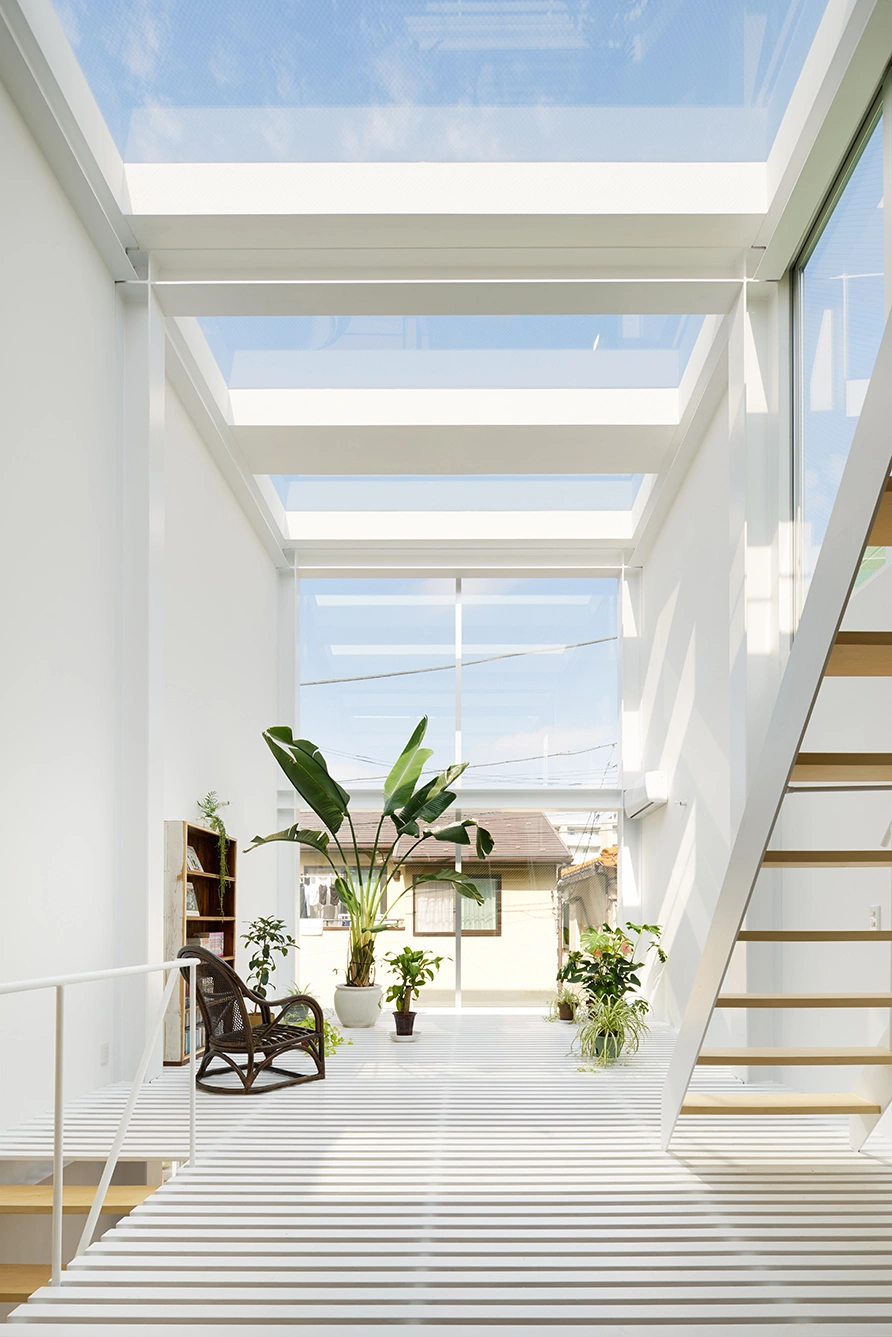 House in Kawasaki by Taichi Mitsuya & Associates — A double-height glazed atrium flooded with natural light through continuous skylight strips, their horizontal mullions creating a rhythmic grid pattern...