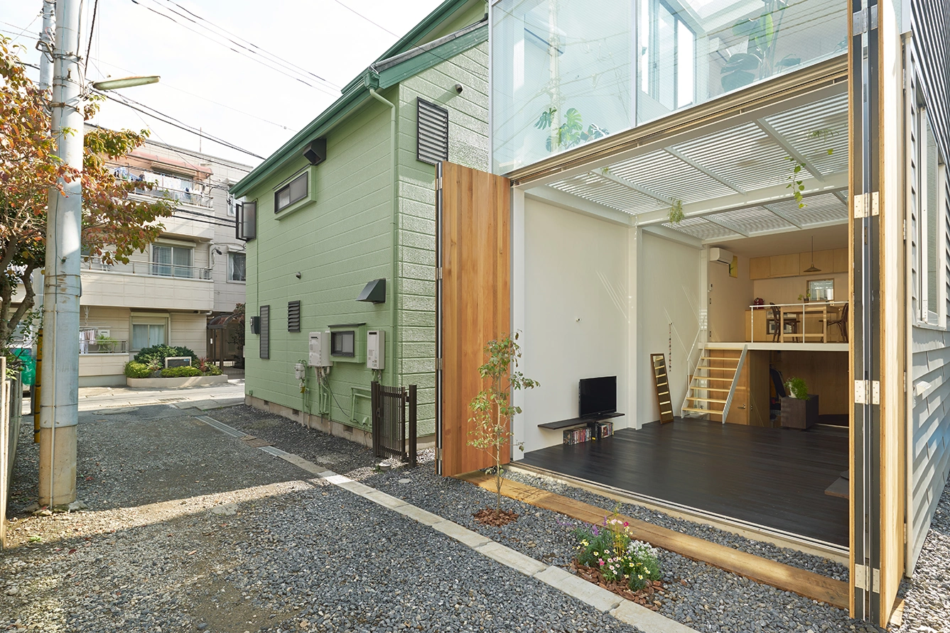 House in Kawasaki by Taichi Mitsuya & Associates — The folding timber doors in warm wood tone frame the open threshold, revealing the interior's dark charcoal flooring and light-filled upper volumes.