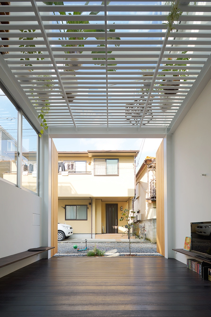House in Kawasaki by Taichi Mitsuya & Associates — A deep interior view frames the house's primary spatial strategy: a nine-meter-high glazed volume with horizontal aluminum mullions creating a regular grid...