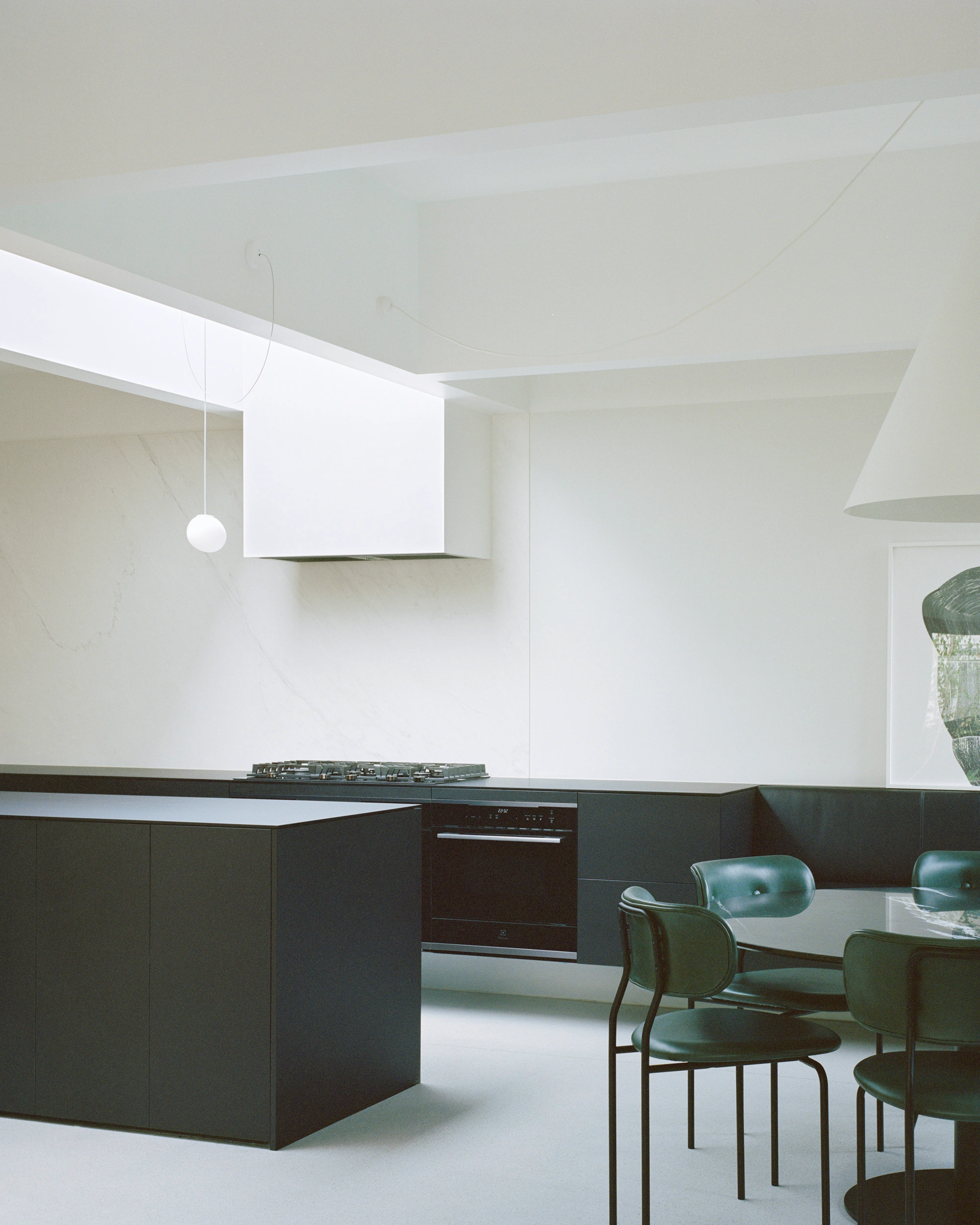 House K by Kart Projects — The kitchen interior demonstrates a deliberate material contrast: charcoal-black timber cabinetry forms a robust L-shaped volume anchoring the space, while...