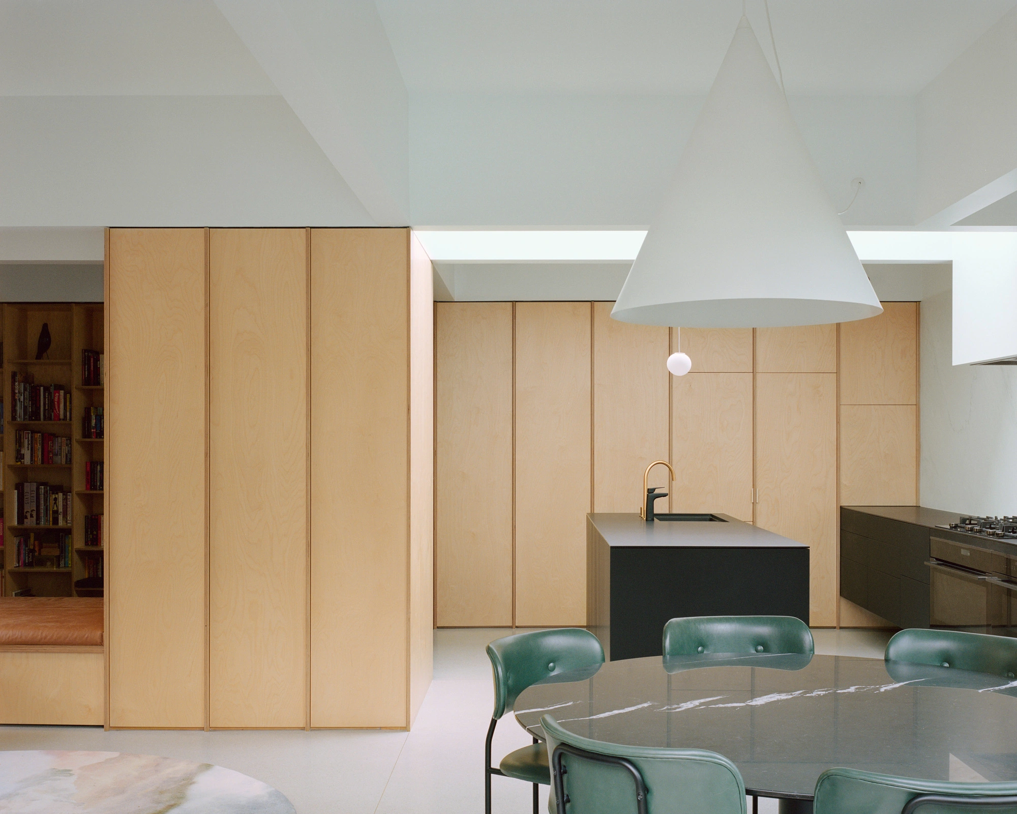 House K by Kart Projects — House K's kitchen extension demonstrates material restraint through continuous birch plywood cabinetry that wraps the perimeter, creating visual continuity...