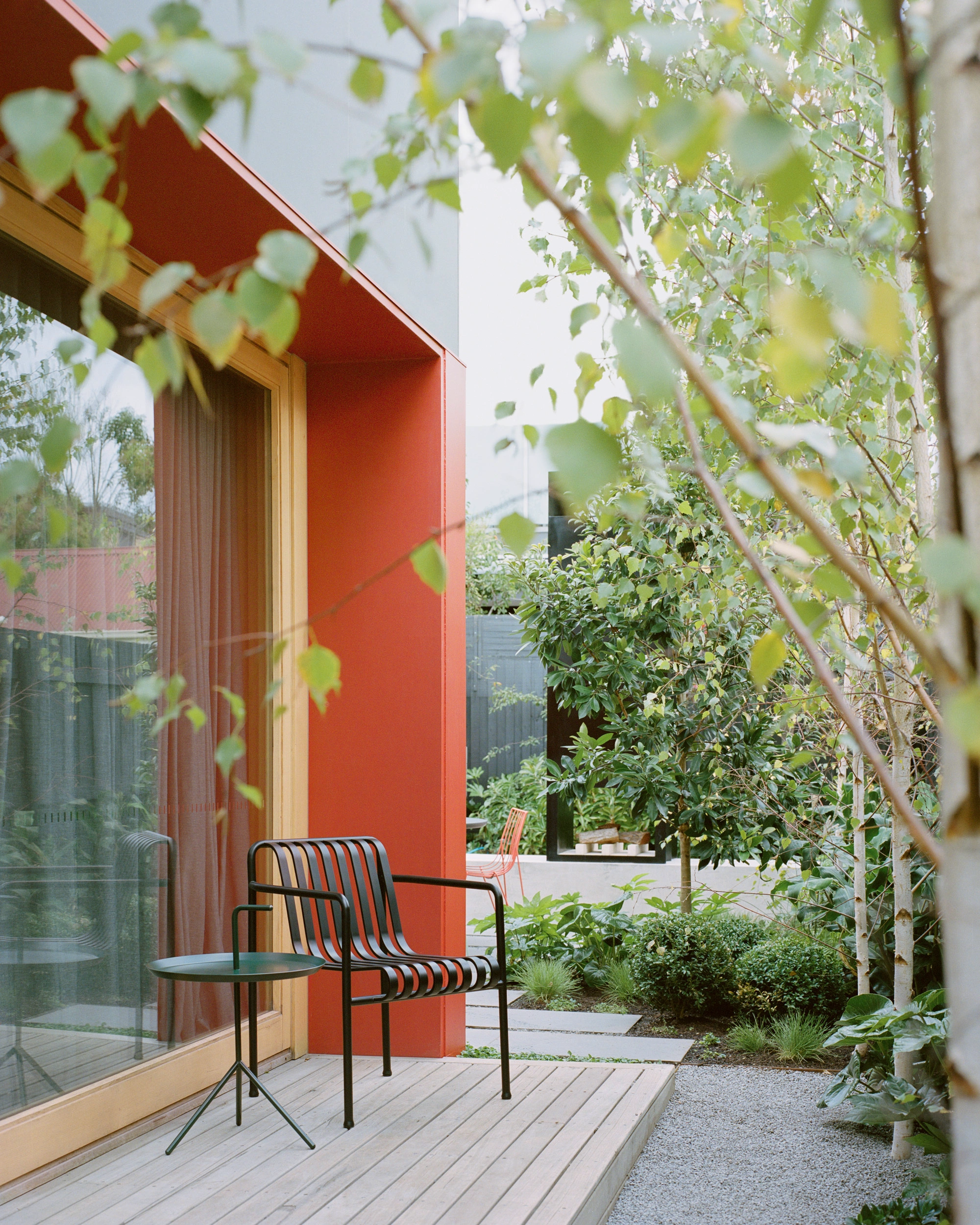 House K by Kart Projects — A lean extension punctuates the garden threshold with a vibrant terracotta-rendered wall featuring vertical ribbed panel divisions.