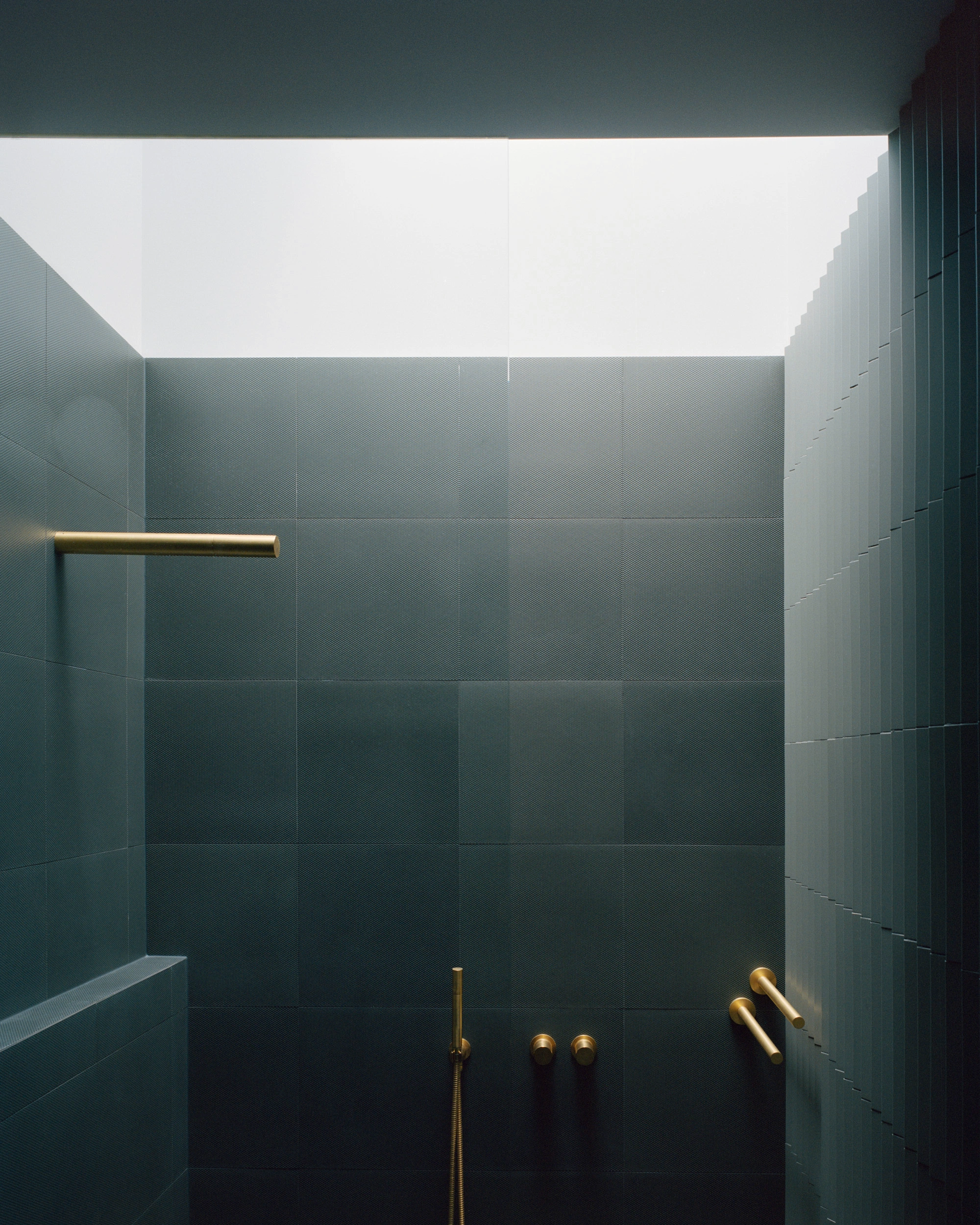 House K by Kart Projects — A wet bathroom interior featuring dark slate-grey tile cladding arranged in a grid pattern across floor-to-ceiling walls.