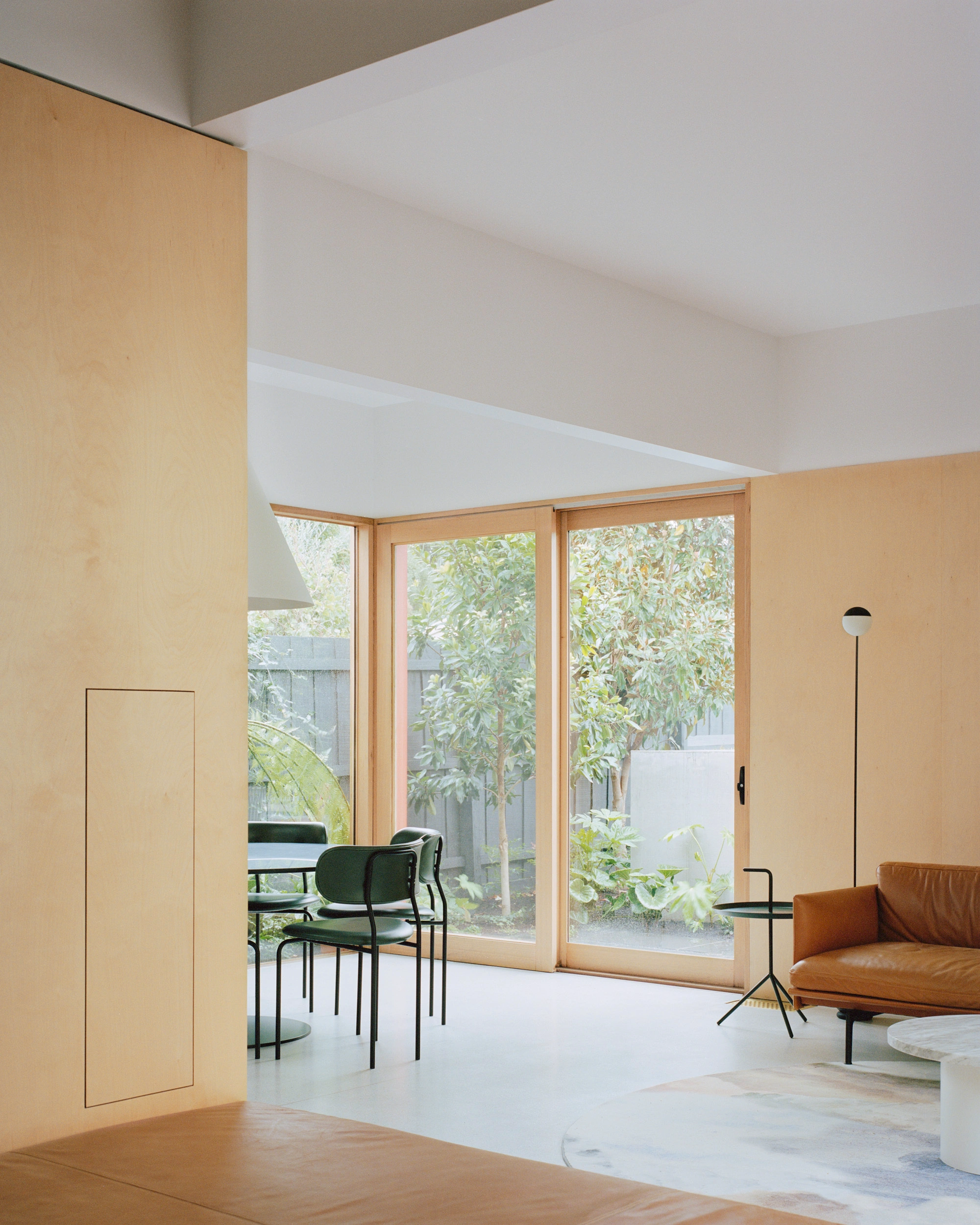 House K by Kart Projects — A timber-framed glazed threshold opens onto a courtyard garden, with three substantial glass panels set in natural wood frames revealing mature trees beyond.
