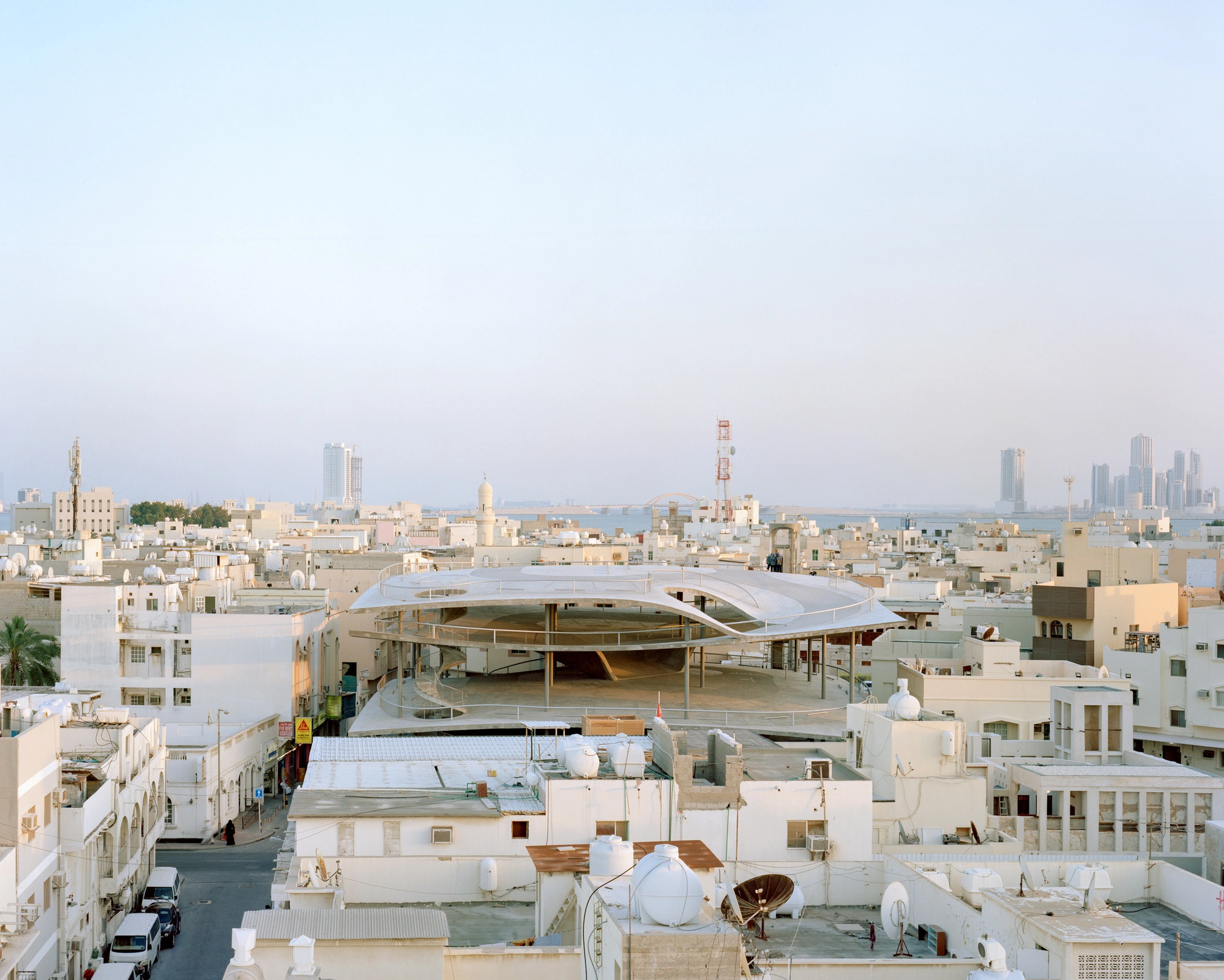 Pearling Path's Four Car Parks by Christian Kerez — A curved concrete car park rises prominently from Muharraq's dense medieval urban fabric, its pitched roof cantilevering dramatically over the surrounding...