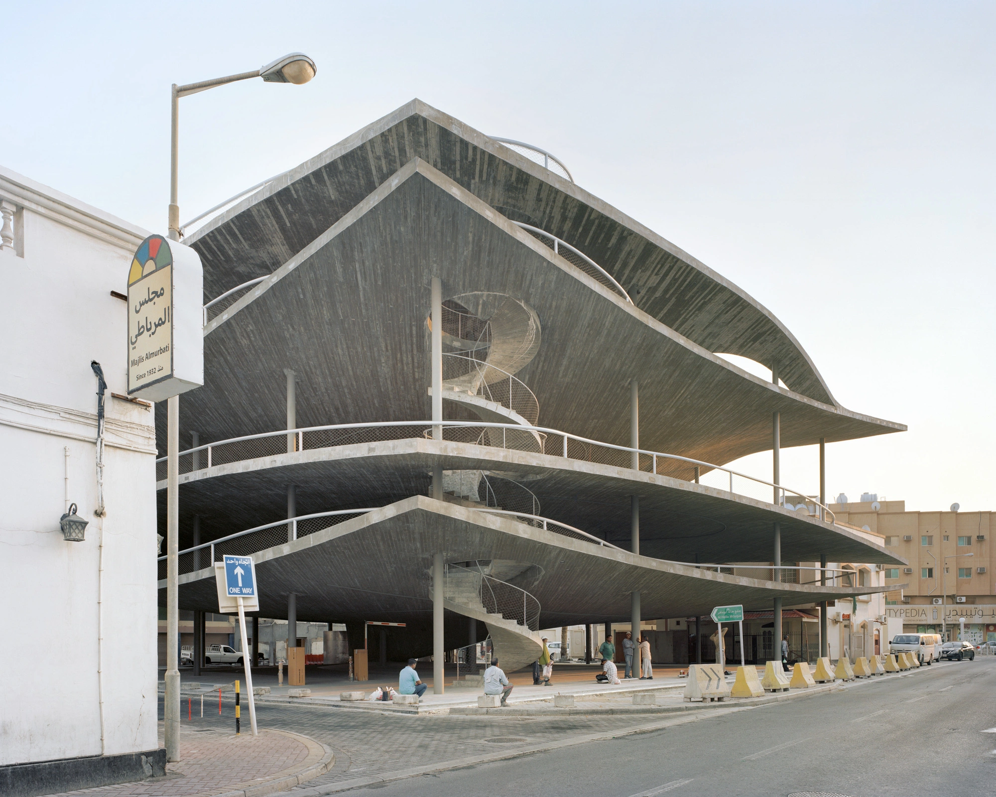 Pearling Path's Four Car Parks by Christian Kerez — A spiraling concrete car park in Muharraq's historic center, photographed from street level to reveal its dramatic pitched roof with curved edges...
