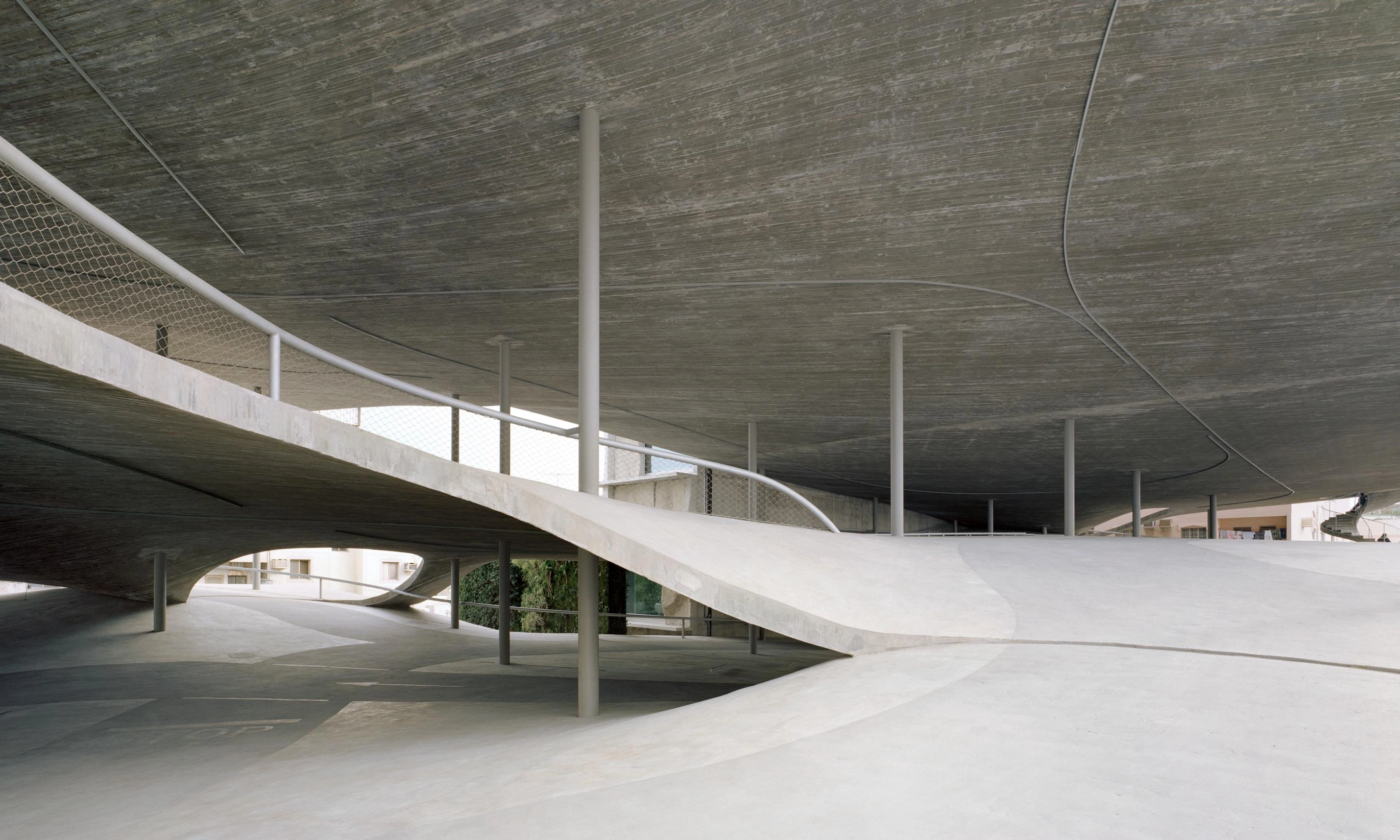 Pearling Path's Four Car Parks by Christian Kerez — The photograph captures the underside of a monolithic concrete structure, where a dramatically cantilevered pitched roof extends over an open ground-level...