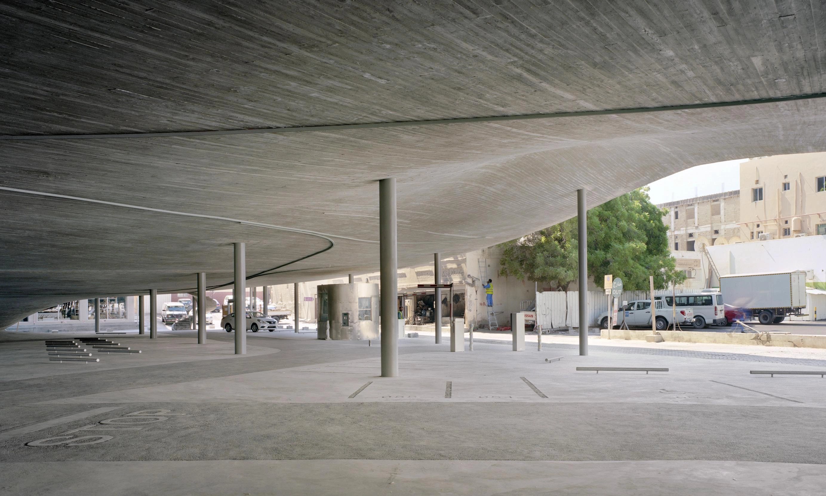 Pearling Path's Four Car Parks by Christian Kerez — A cavernous ground-level plaza beneath a dramatically cantilevered concrete roof, its pitched form visible through the open perimeter.