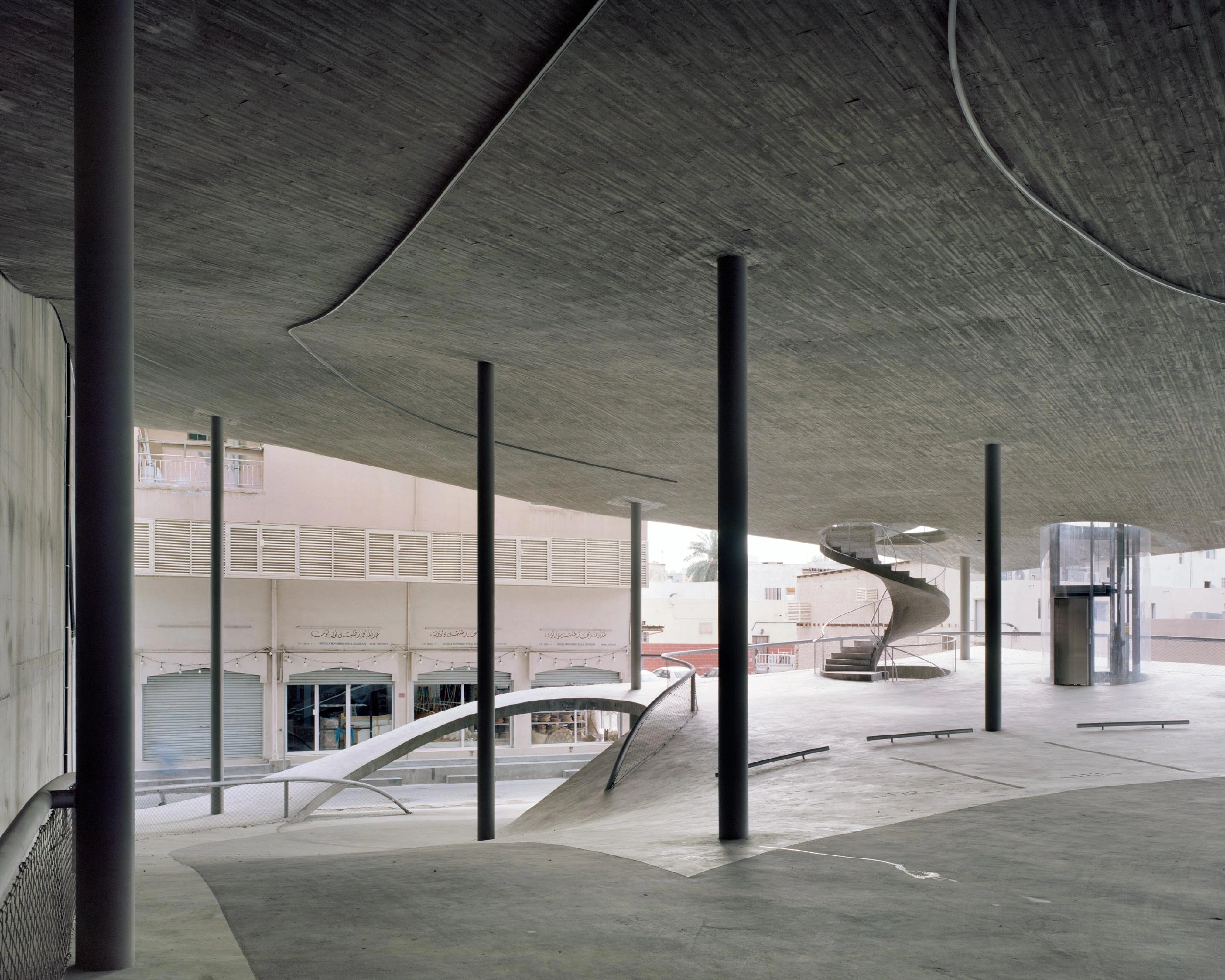 Pearling Path's Four Car Parks by Christian Kerez — A ground-level threshold beneath a dramatically cantilevered pitched-roof structure in exposed concrete.