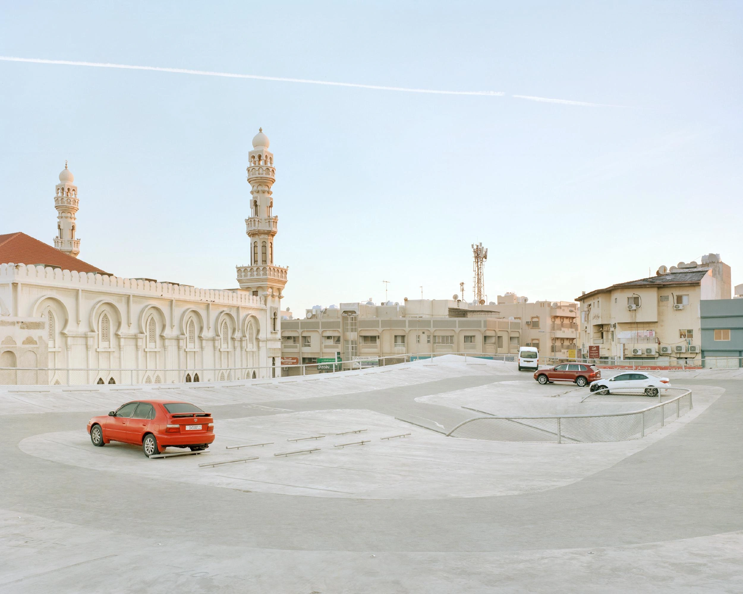 Pearling Path's Four Car Parks by Christian Kerez — A sprawling concrete plaza fronts the car park's monolithic facade, its expansive horizontal expanse punctuated by a red sedan positioned in the foreground.