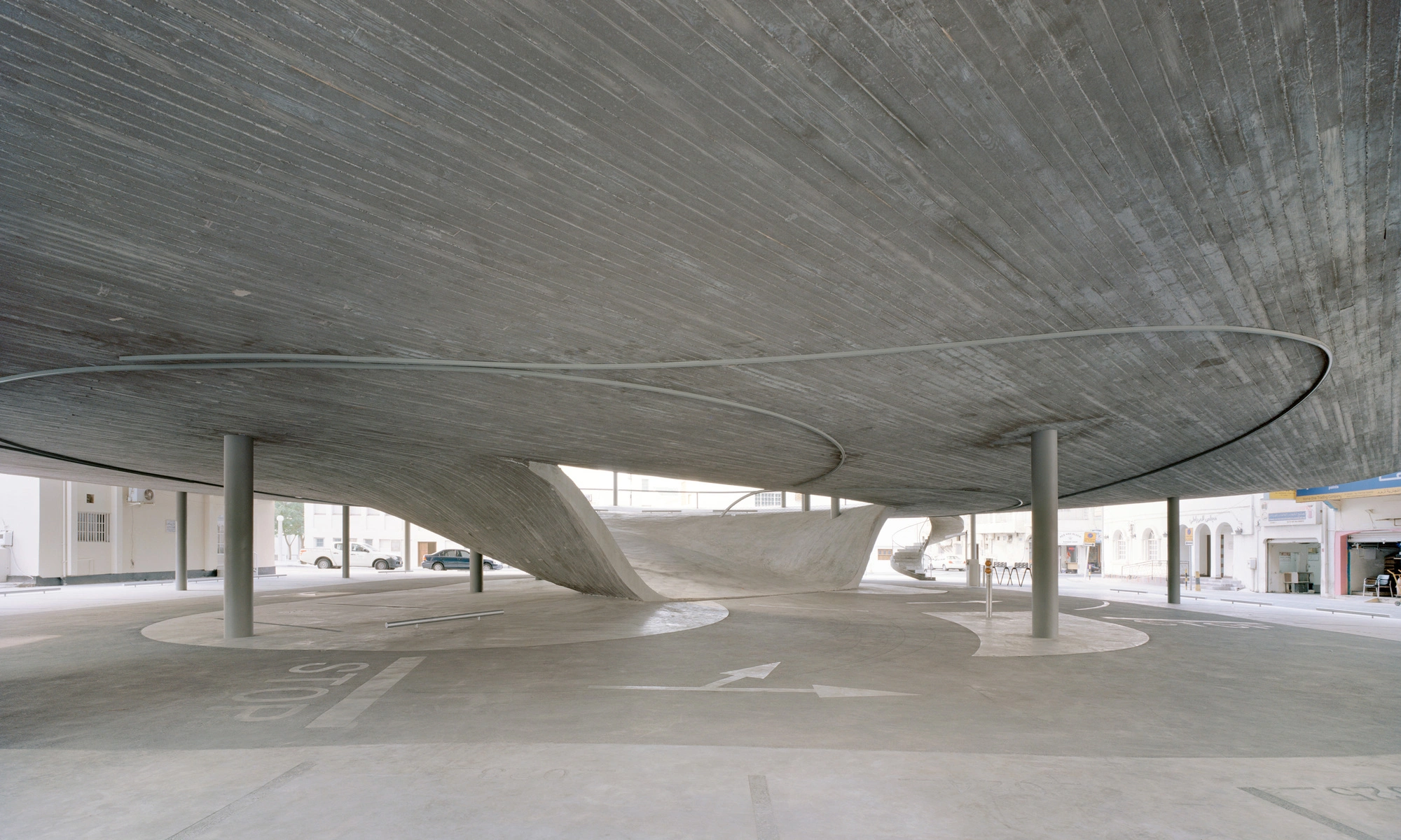 Pearling Path's Four Car Parks by Christian Kerez — A monolithic concrete structure dominates this ground-level plaza, its pitched roof form curving upward with dramatic cantilevers that extend beyond...
