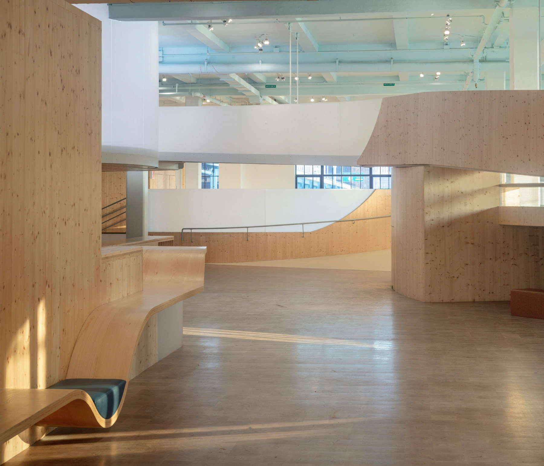 Bronx Children's Museum by O'Neill McVoy — A double-height gallery interior defined by sculptural timber walls in light pine with visible knots throughout.