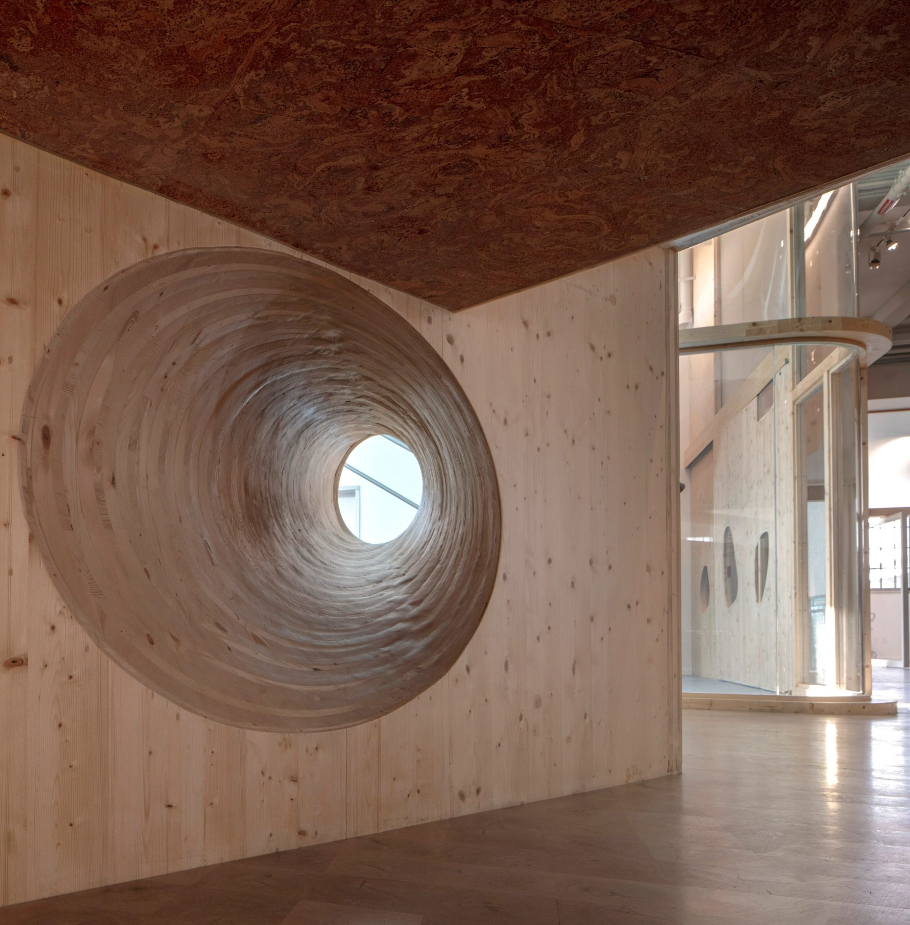 Bronx Children's Museum by O'Neill McVoy — A timber-lined interior chamber features a dramatic spiral tunnel carved through a pine wall, its concentric rings creating a hypnotic vortex toward a...
