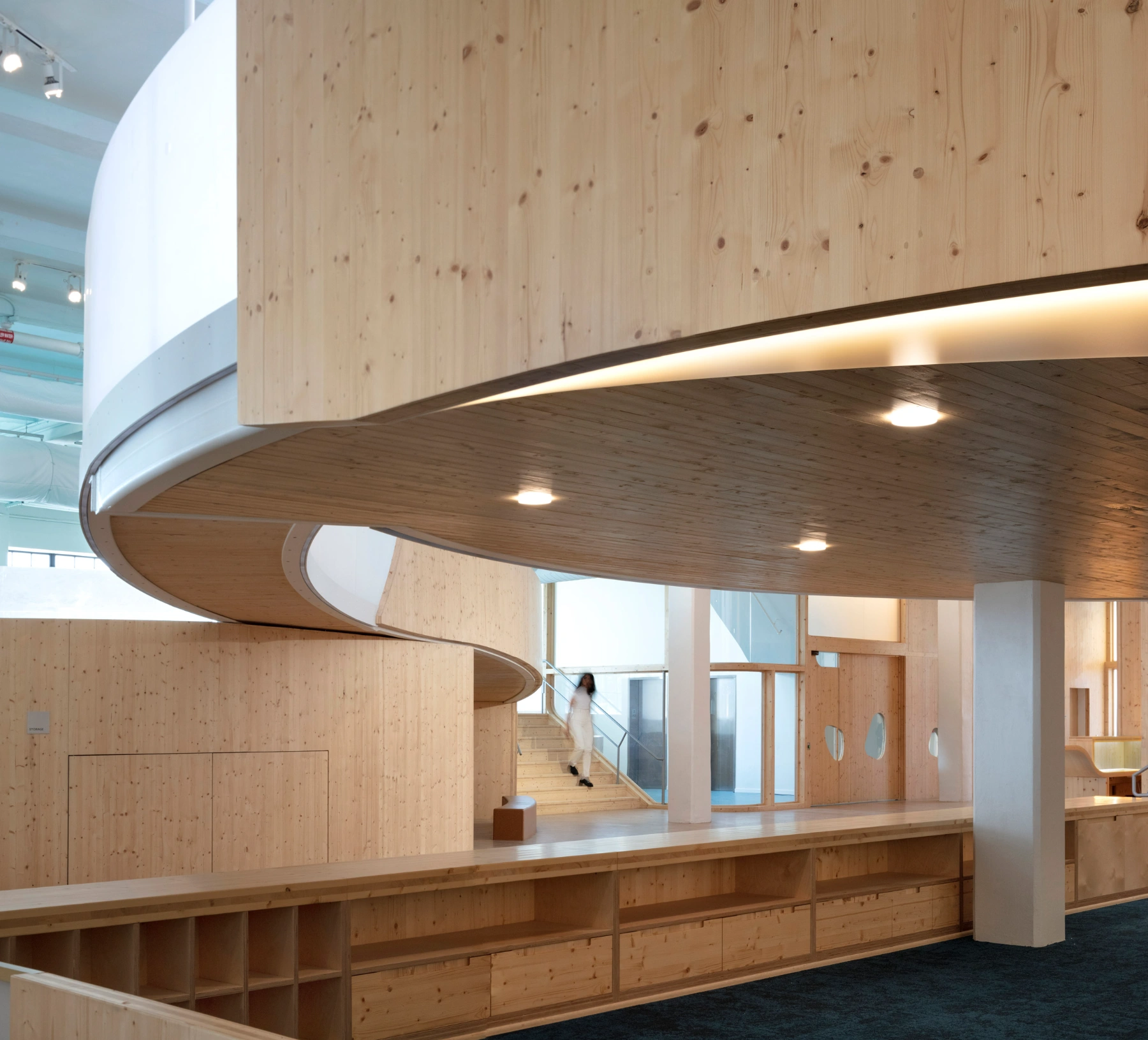 Bronx Children's Museum by O'Neill McVoy — A spiral timber tunnel carved through a light pine wall creates a sculptural void that frames bright sky beyond, establishing a strong backlit threshold.