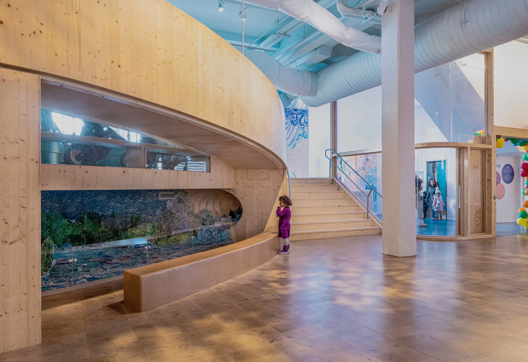 Bronx Children's Museum by O'Neill McVoy — A curved timber wall dominates the foreground, its light pine surface marked with prominent knots and natural grain.