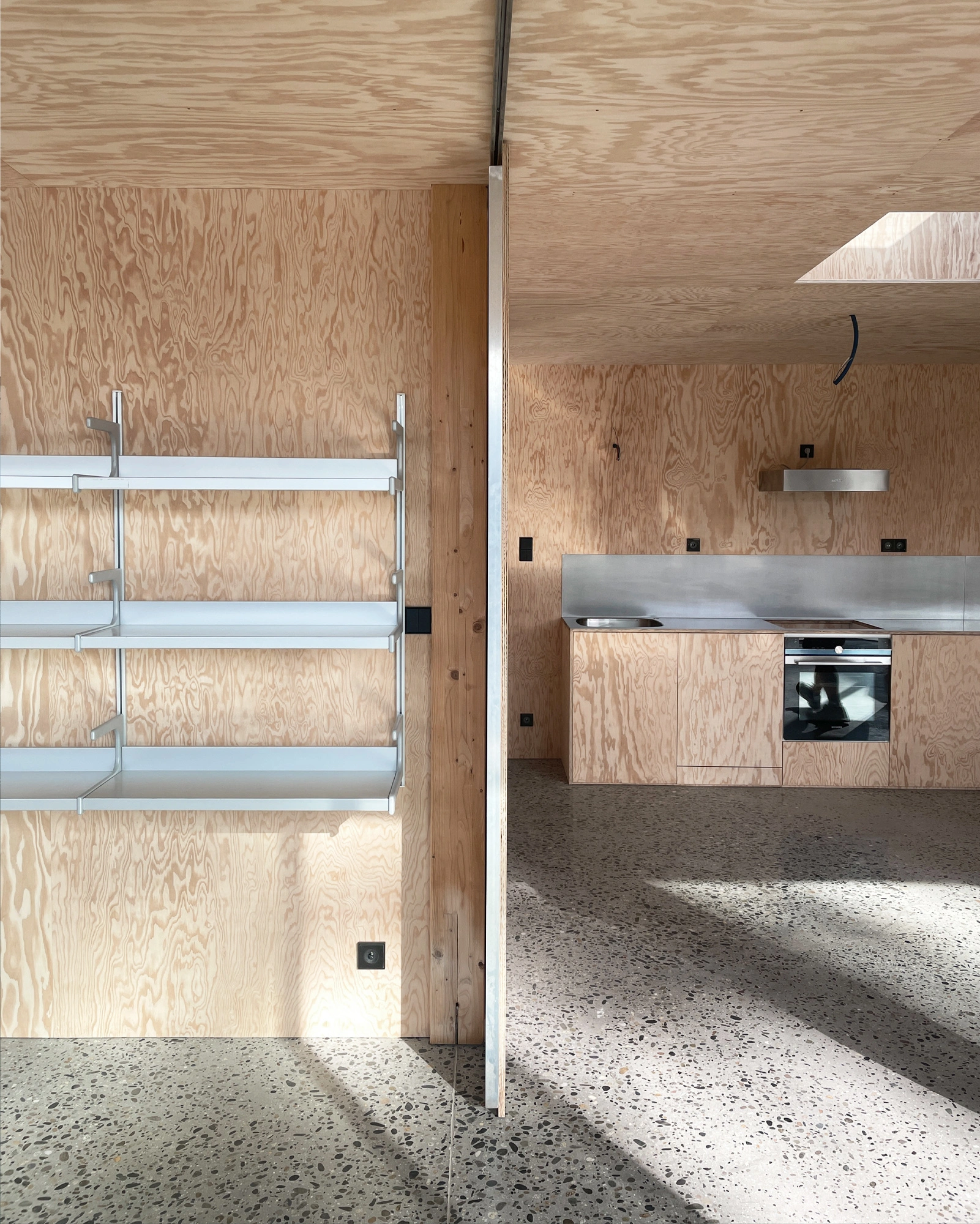 M37 House by BAST + littoral — Interior view of the M37 House kitchen and living space, framed through a translucent glass partition.