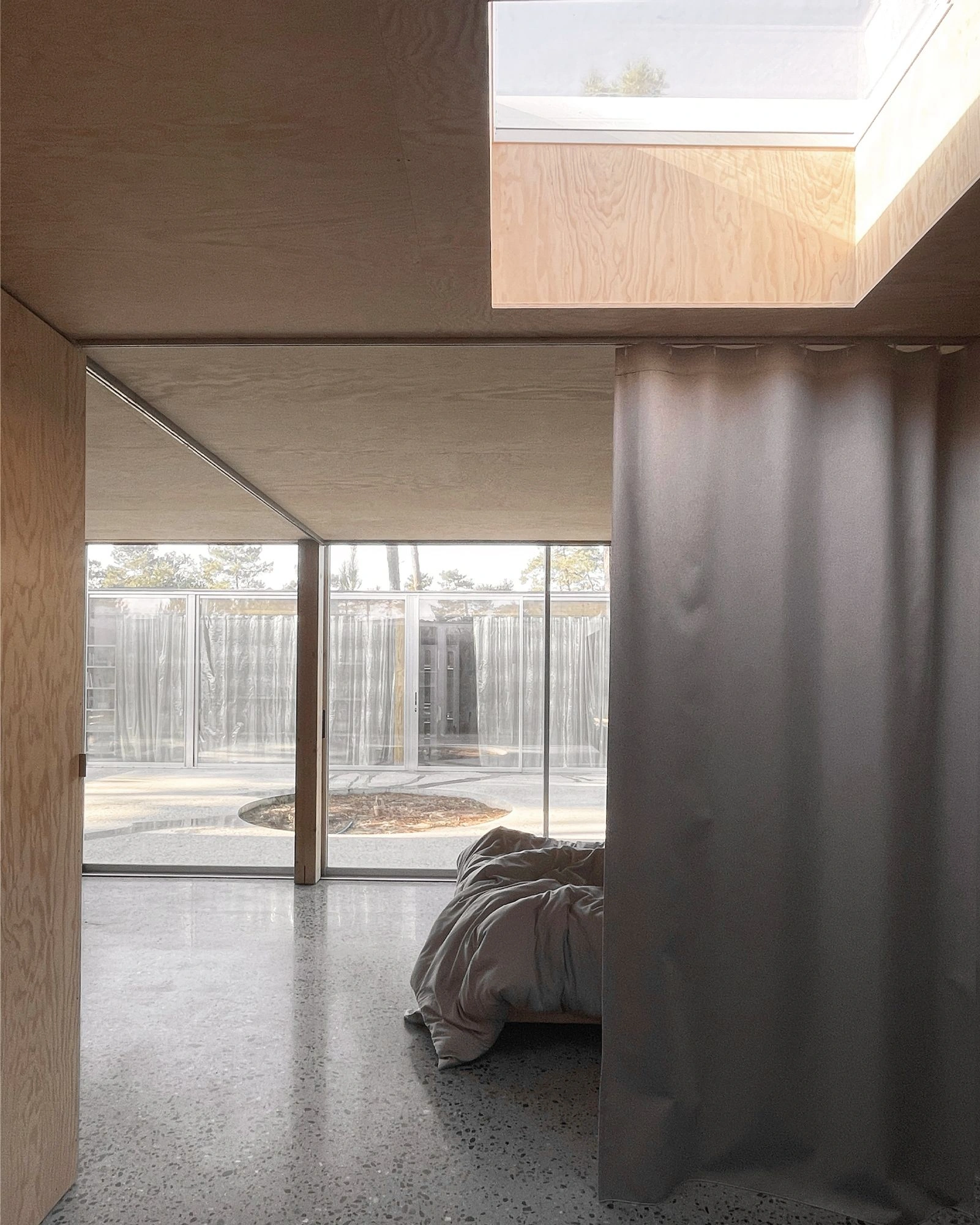 M37 House by BAST + littoral — Interior threshold framed by a tall charcoal fabric curtain, with polished concrete flooring extending into an open courtyard beyond.