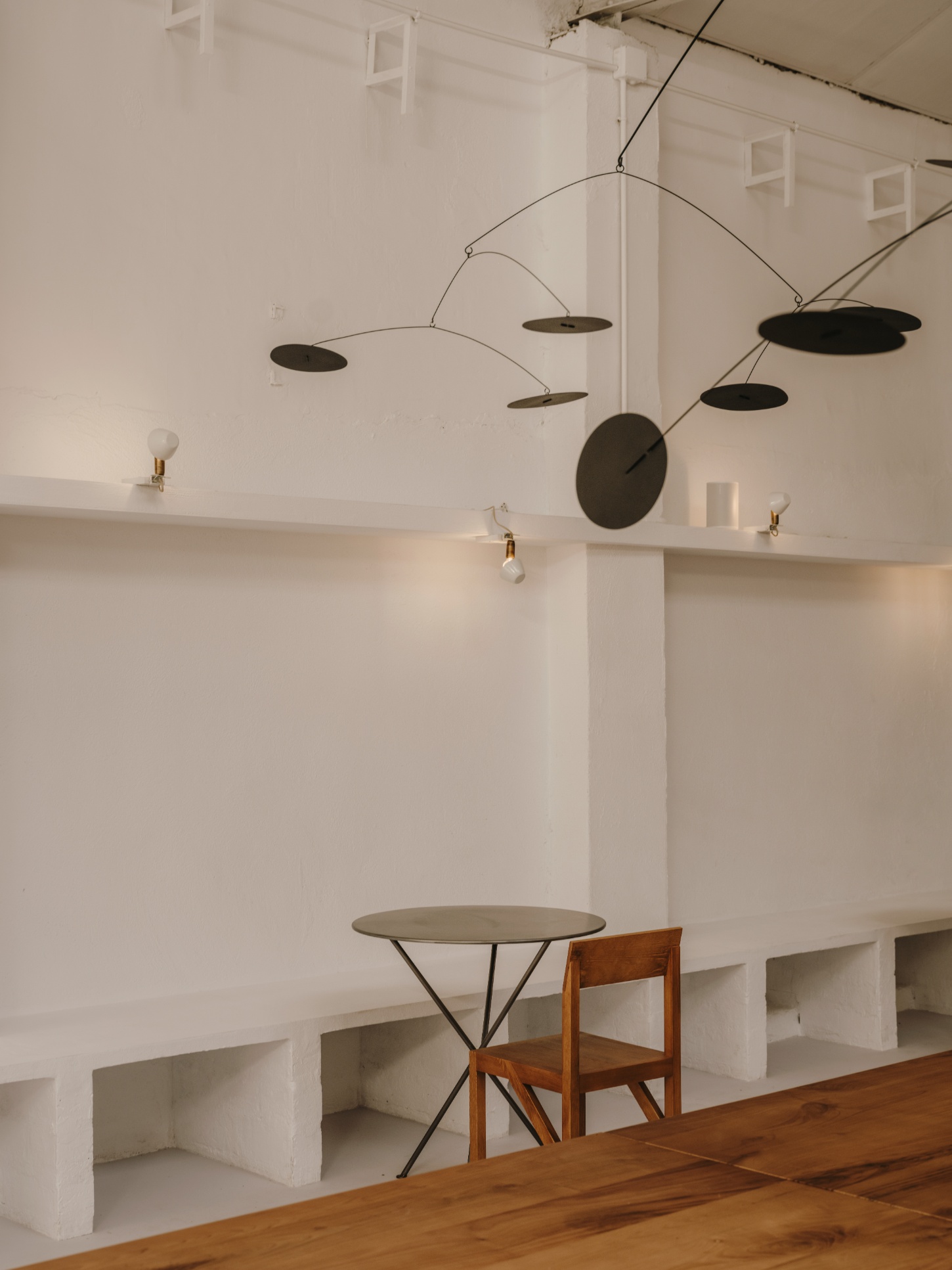 Alma Nomad by Plantea Studio by Plantea Estudio — A minimal dining vignette suspended beneath a sculptural mobile suspended from the ceiling.