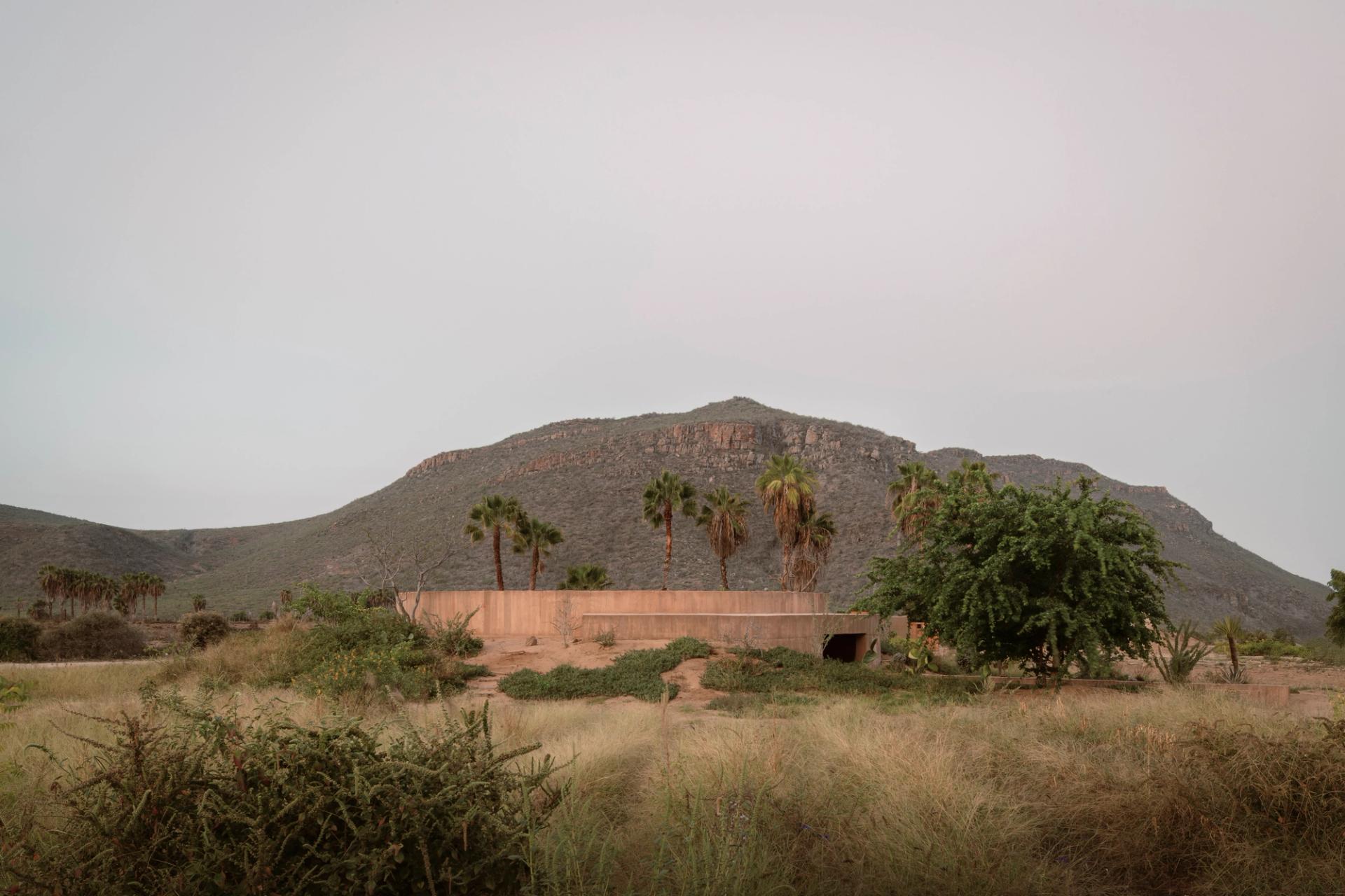 Spiritual Enclosure by Ruben Valdez — A monolithic concrete enclosure anchors the desert landscape of Todos Santos, its curved walls rendered in warm terracotta-grey concrete framing the...