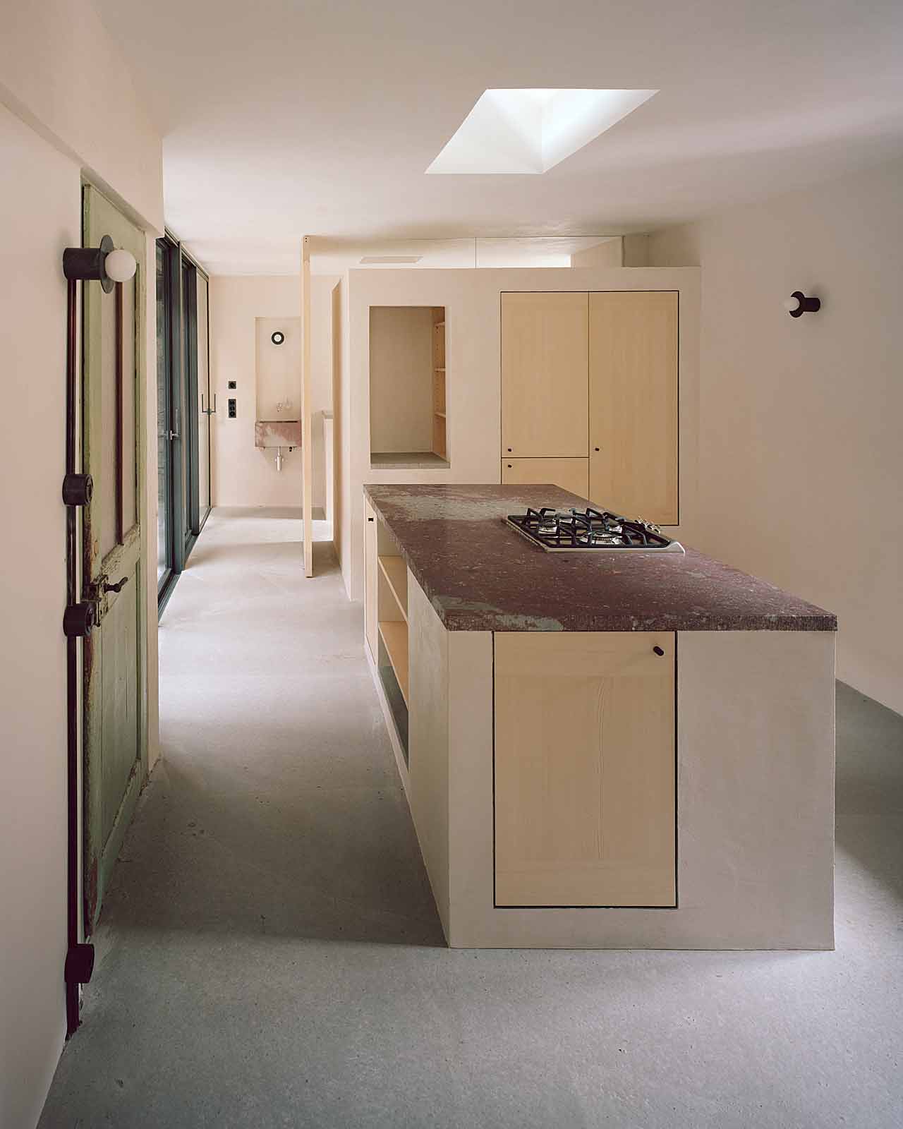 Mühle Ennenda by Atelier Lando Rossmaier — A galley kitchen occupies the longitudinal passage of the converted mill, defined by a linear island with dark terrazzo countertop and integrated gas cooktop.
