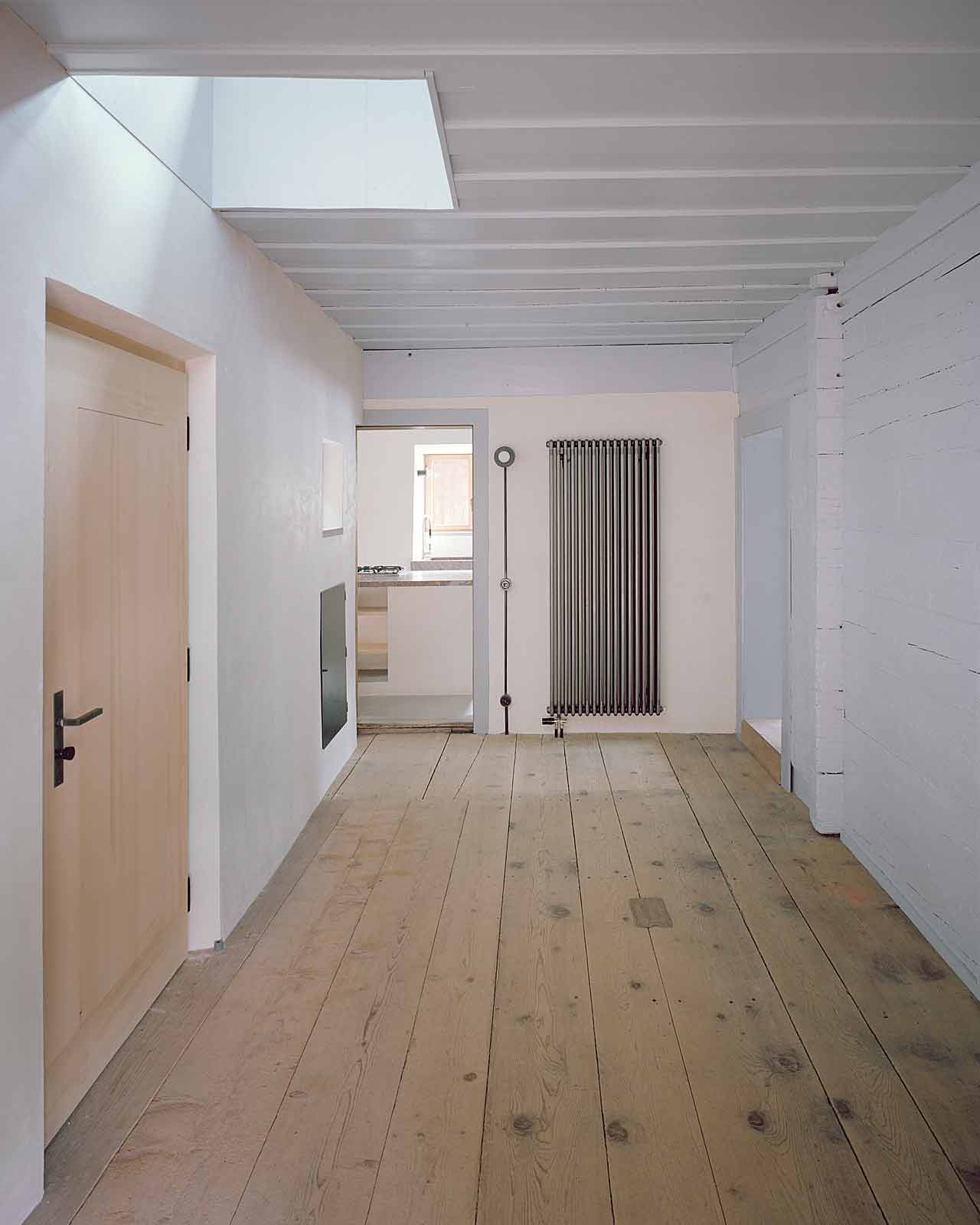 Mühle Ennenda by Atelier Lando Rossmaier — A longitudinal corridor reveals the methodical undoing of a mill's interior, where newly installed timber ceiling beams span above whitewashed walls bearing...