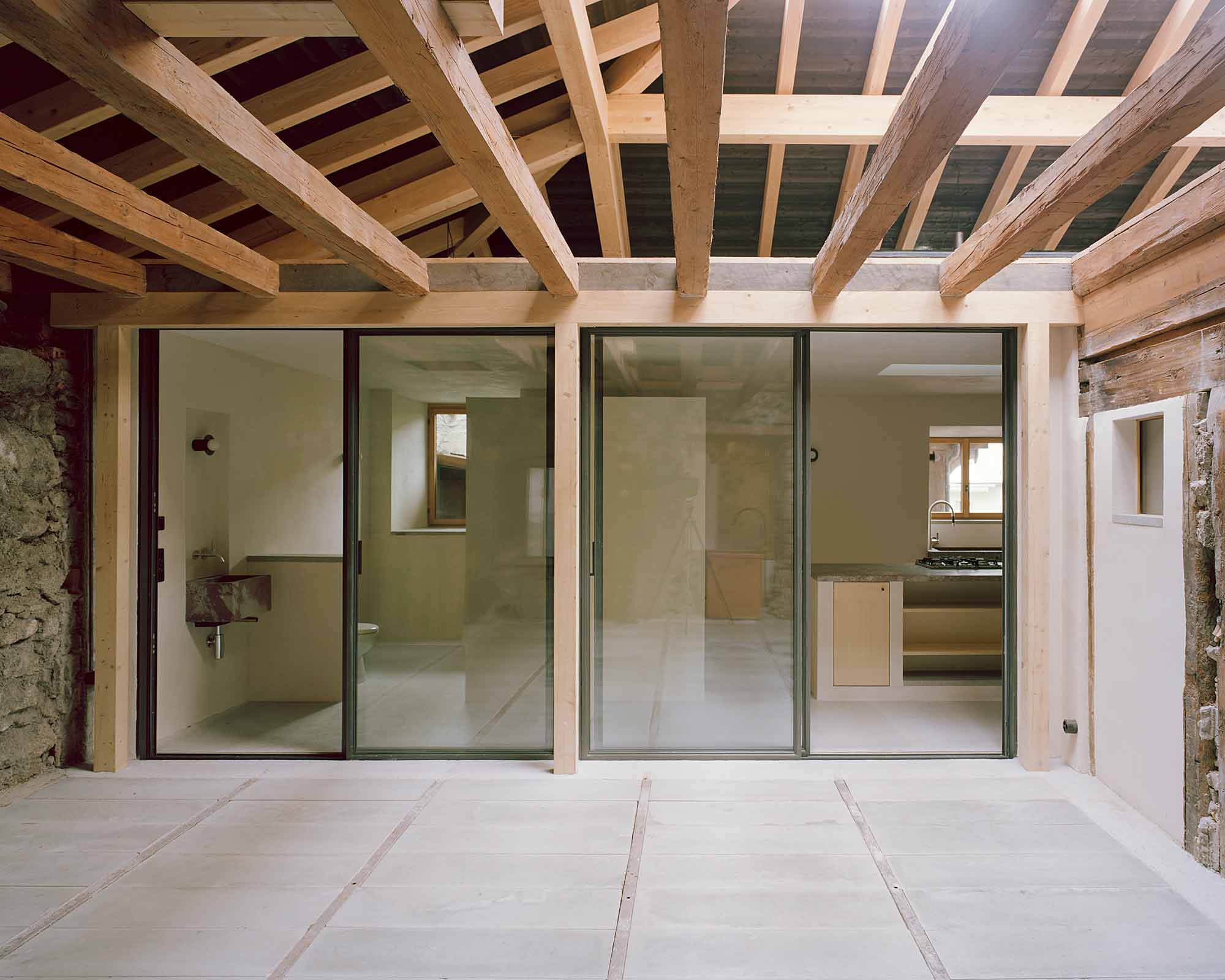 Mühle Ennenda by Atelier Lando Rossmaier — A threshold space revealing the project's palimpsestic approach: newly installed timber ceiling beams span above a concrete floor slab, their warm honey...