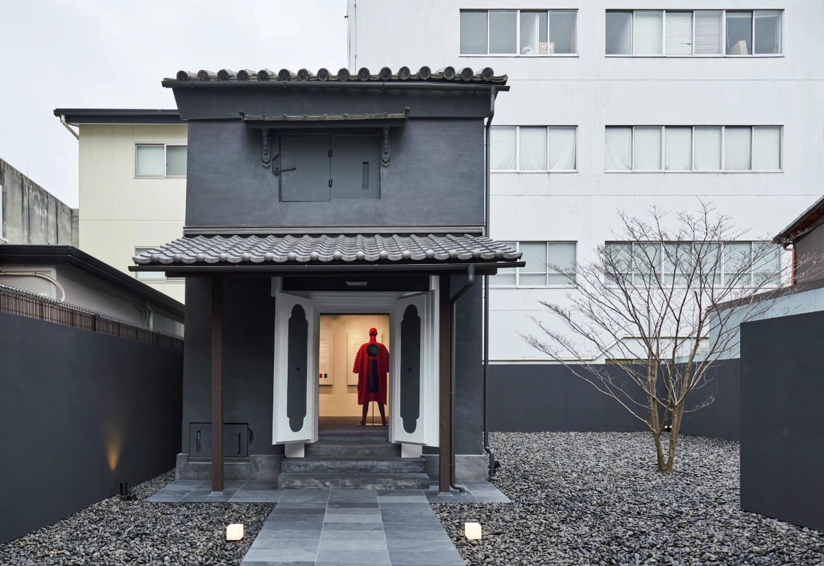 Issey Miyake Kyoto by Naoto Fukasawa Design — The storefront entrance features a recessed threshold framed by a white plaster surround with curved vertical pilasters, set within the dark timber...