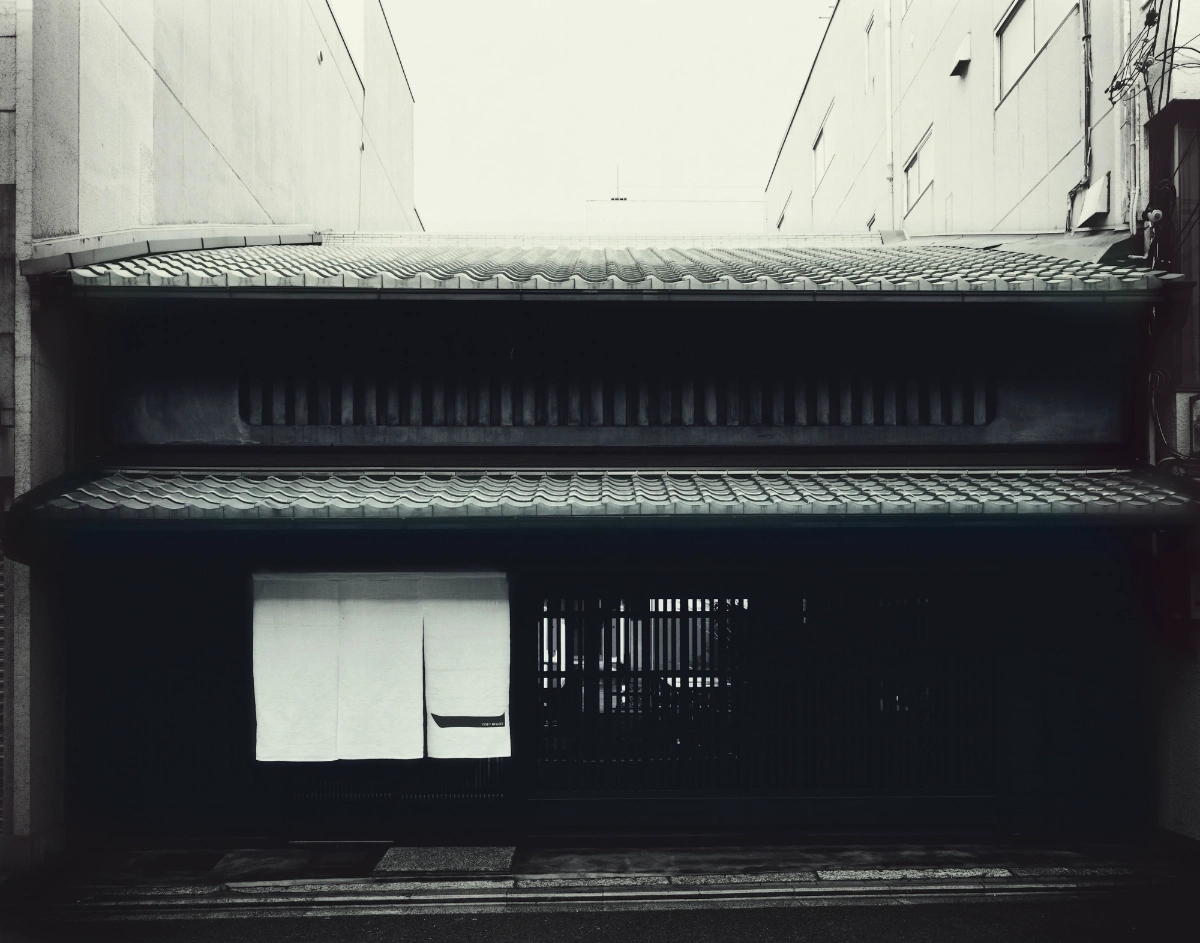 Issey Miyake Kyoto by Naoto Fukasawa Design — The storefront elevation presents a recessed facade deeply shadowed by overhanging timber lattice screens with vertical slat divisions.