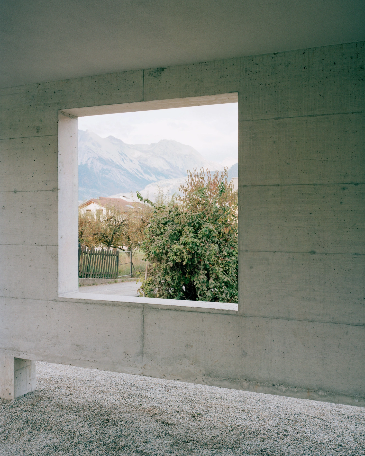 The Wandering House by Lionel Ballmer — A framed view through a square aperture cut into board-formed concrete reveals a rural Alpine landscape.