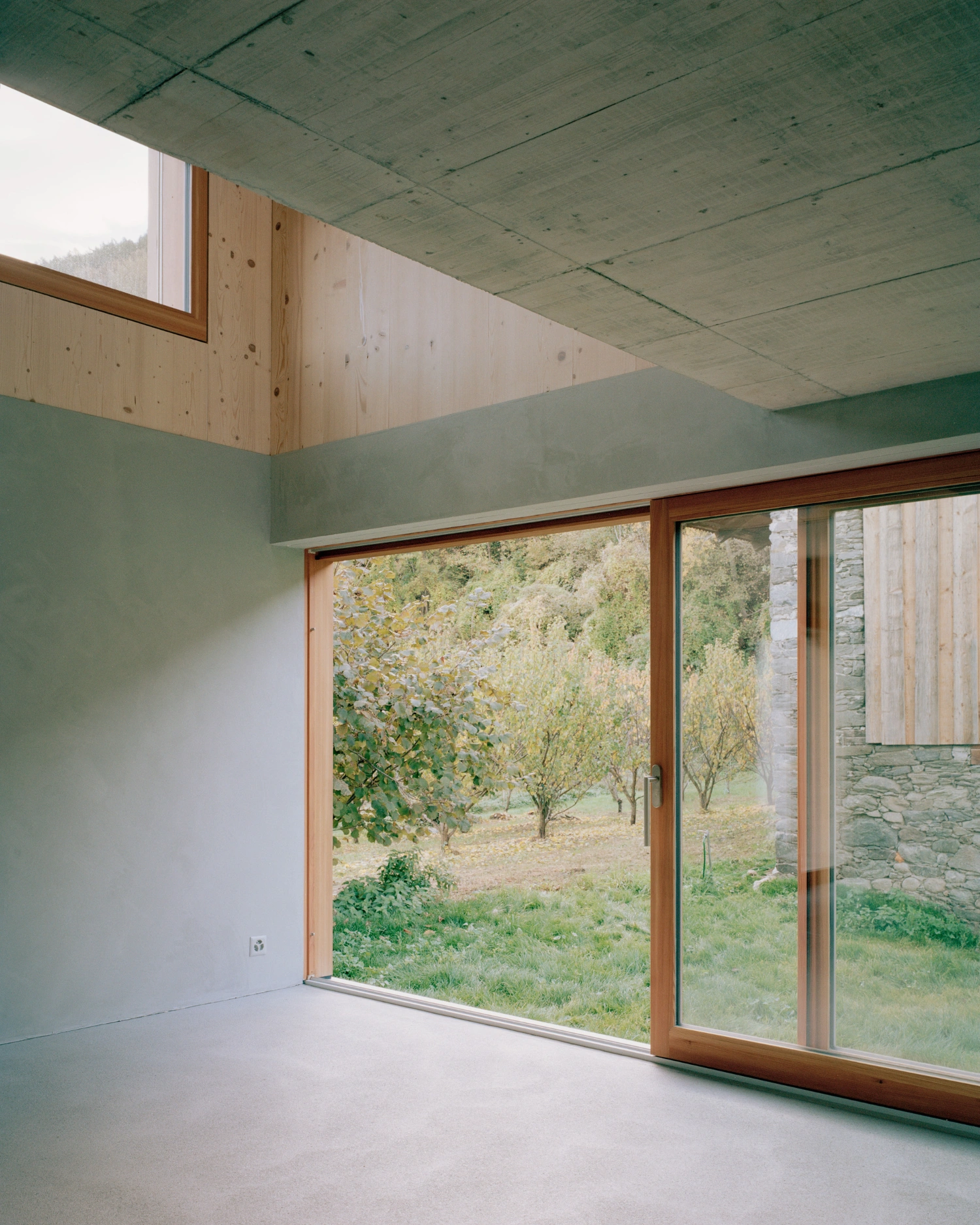 The Wandering House by Lionel Ballmer — Interior view of the elevated volume reveals a minimalist space defined by a continuous timber-framed glazing system that dissolves the boundary between...