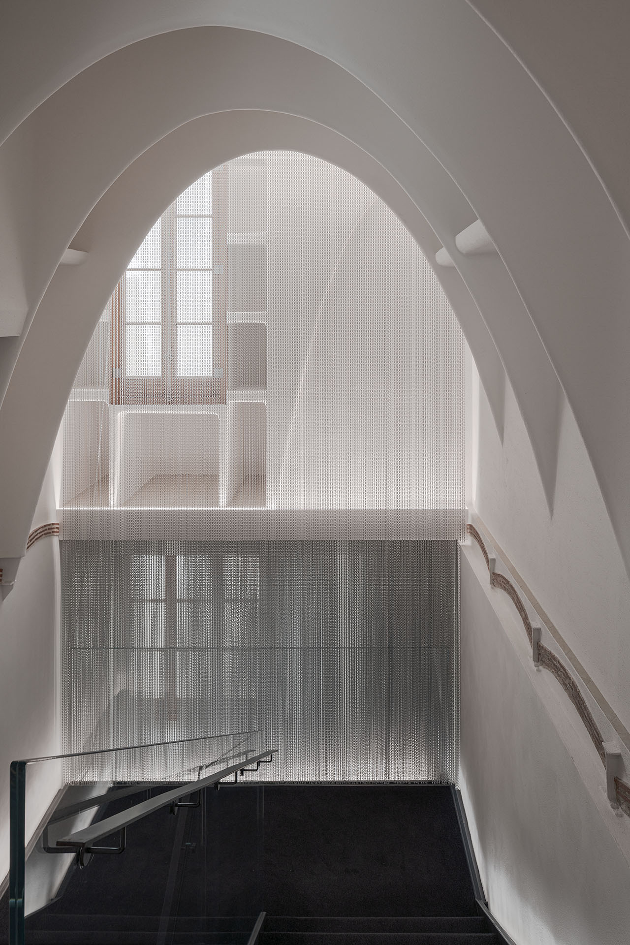 Casa Batlló Stairs & Atrium by Kengo Kuma — A staircase descends into shadow beneath a monumental arched opening, its concrete steps anchored in darkness.