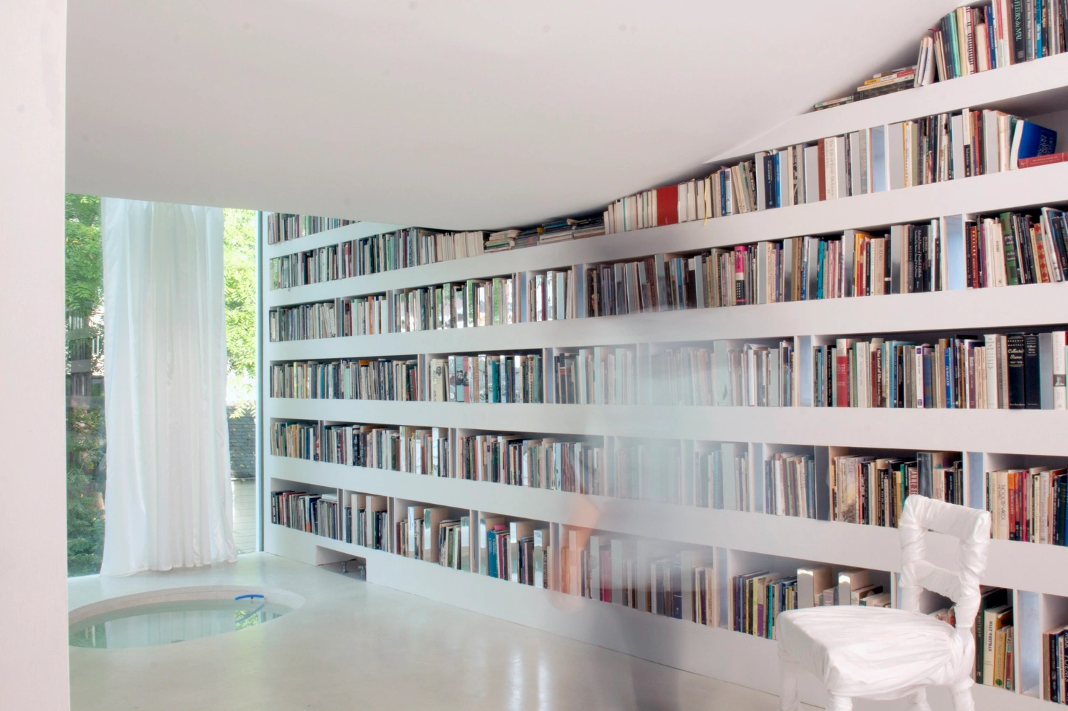 Haffenden House by PARA — A continuous wall of white shelving spans the interior of Haffenden House's library, displaying hundreds of books arranged across six horizontal tiers.