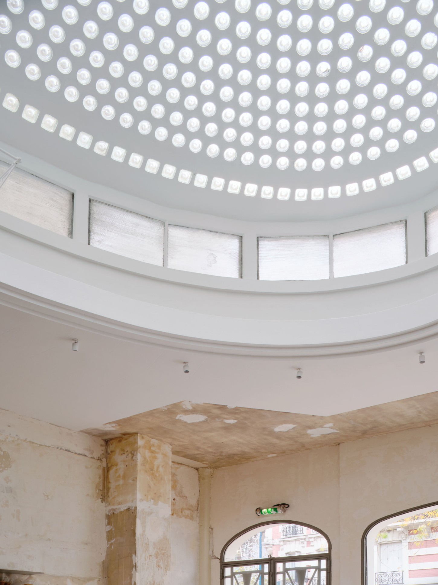 Anbassa by Office Abrami Rojas by Office Abrami Rojas (OAR) — A cylindrical interior space crowned by a coffered ceiling of recessed circular and square luminaires that flood the room with diffuse artificial light.