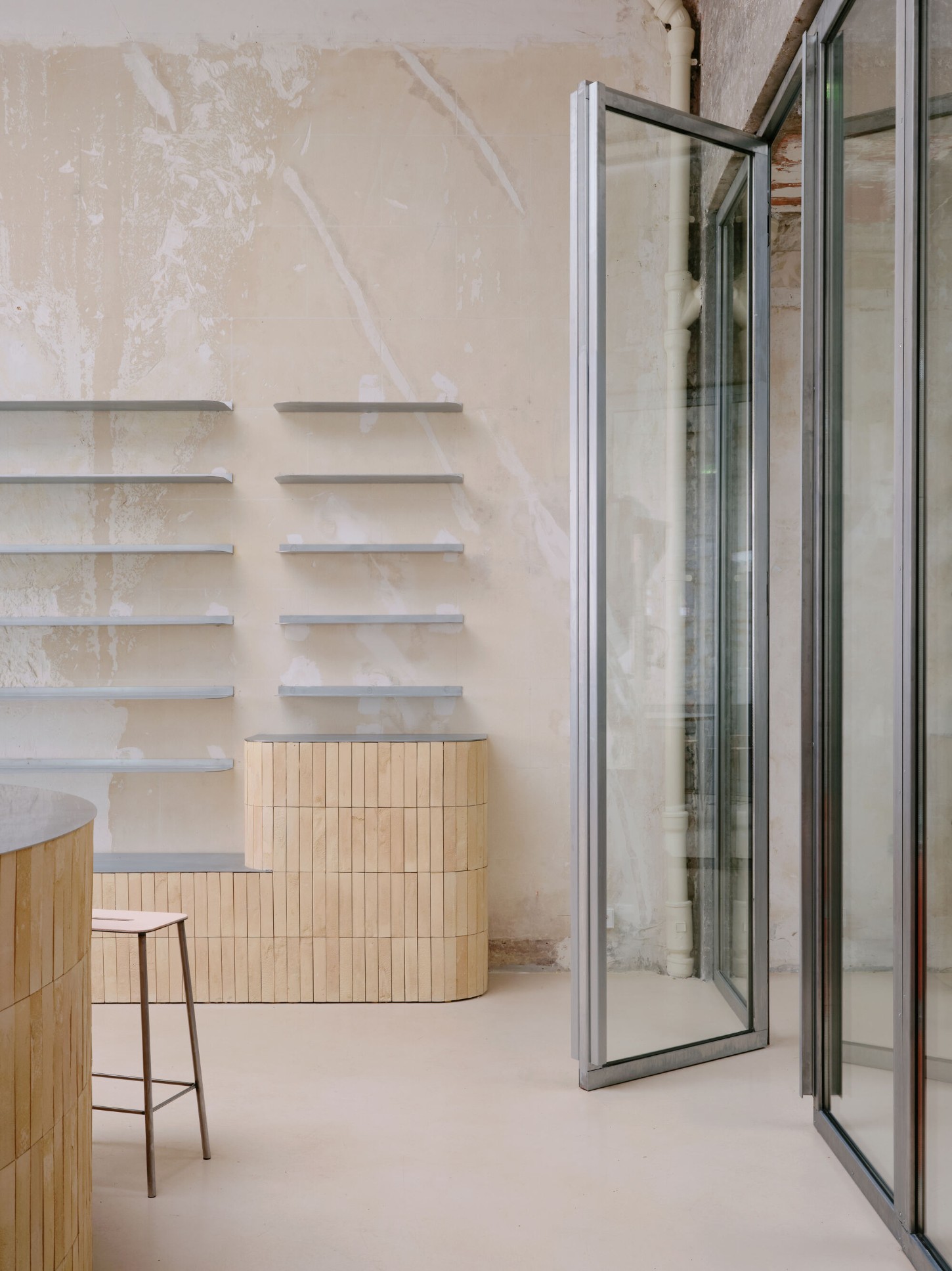 Anbassa by Office Abrami Rojas by Office Abrami Rojas (OAR) — A partially finished interior space showcases timber cabinetry with vertical slat cladding in light wood, positioned beneath a wall of horizontal steel...