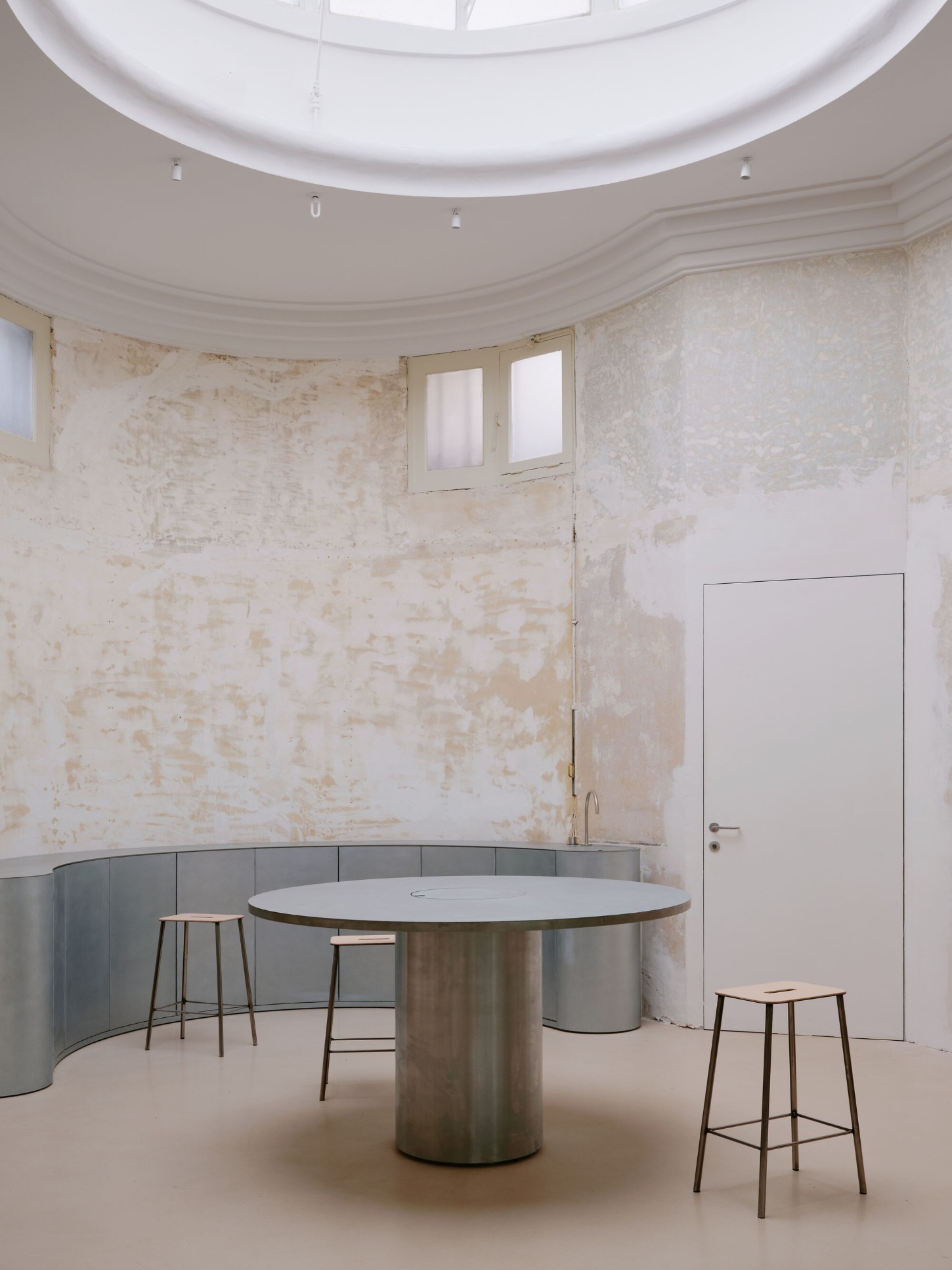 Anbassa by Office Abrami Rojas by Office Abrami Rojas (OAR) — A cylindrical dining table with polished steel base and white marble top anchors this circular interior, its monolithic form echoing the room's geometric...