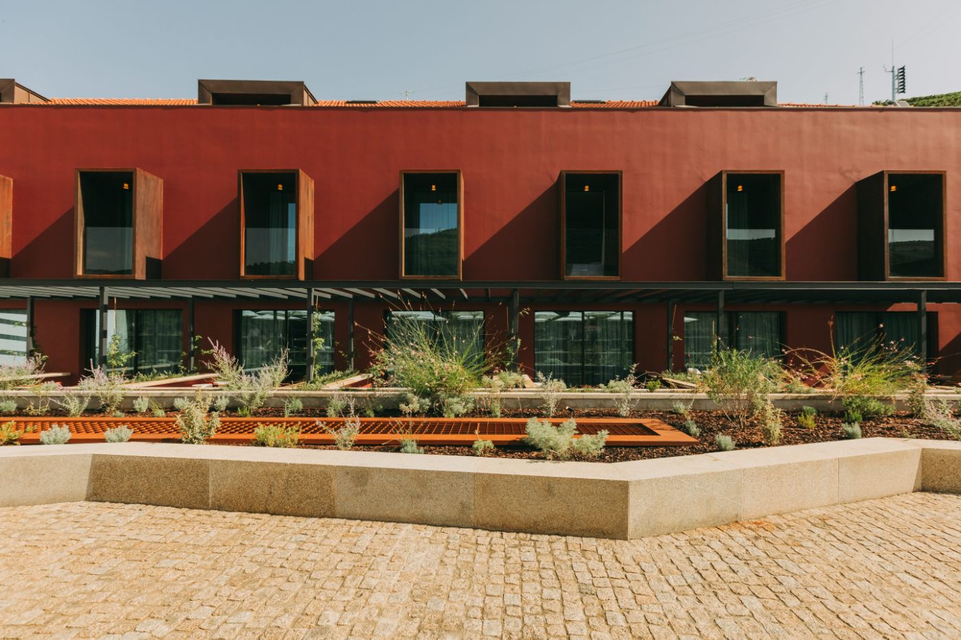 Torel Quinta da Vacaria in Douro Valley by Studio Astolfi and architect Luís Miguel Oliveira — The courtyard elevation reveals a modular facade of rendered terracotta-red walls punctuated by six timber-framed window openings with dark glazing and...