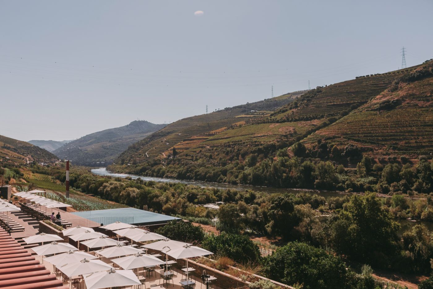 Torel Quinta da Vacaria in Douro Valley by Studio Astolfi and architect Luís Miguel Oliveira — Terraced outdoor dining platform overlooking the Douro Valley, featuring a modular system of cream-colored umbrellas arranged across rammed-earth or...