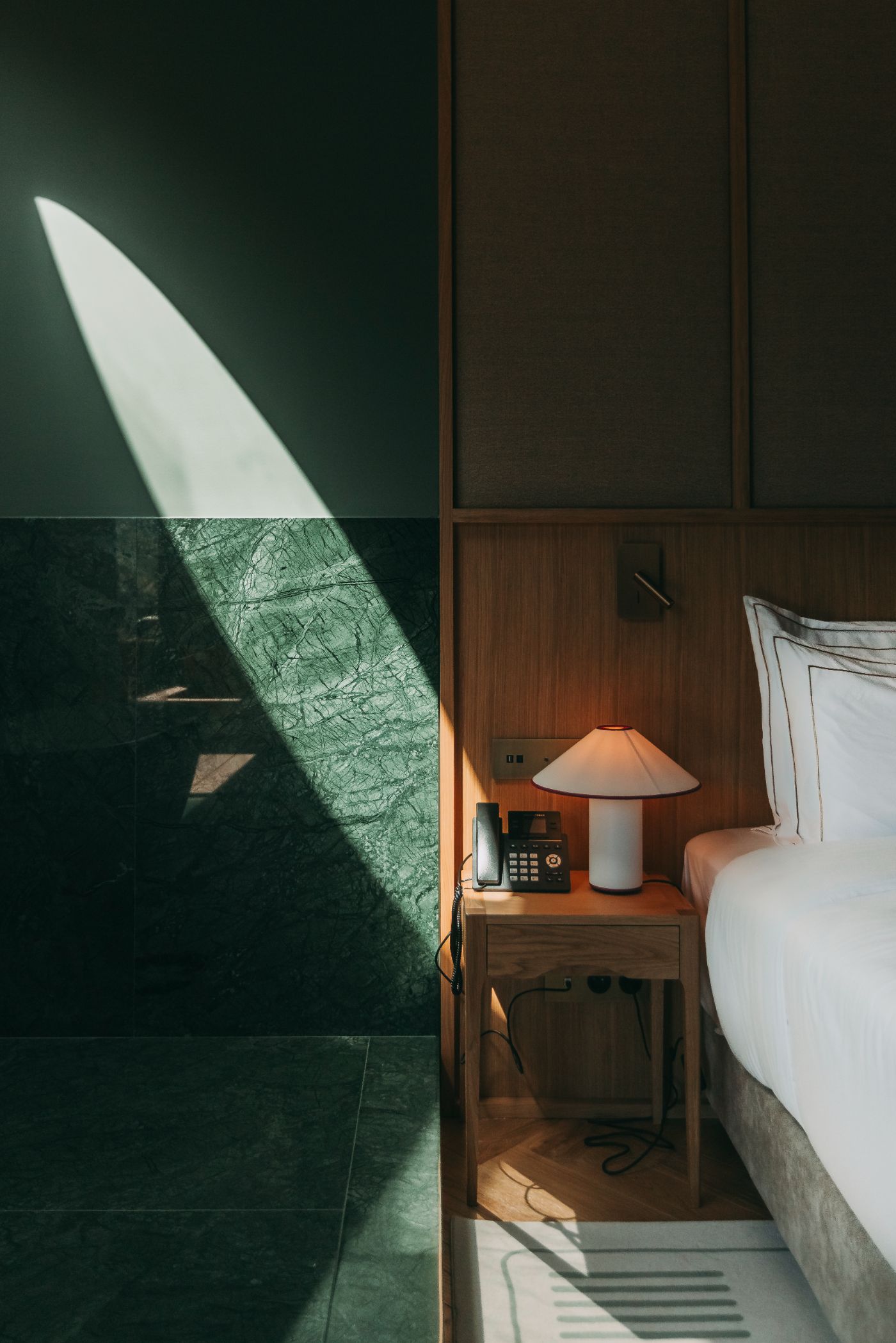 Torel Quinta da Vacaria in Douro Valley by Studio Astolfi and architect Luís Miguel Oliveira — A corner bedroom detail captures afternoon light through a gridded window wall with dark frame, casting geometric shadows across green-tiled surfaces.