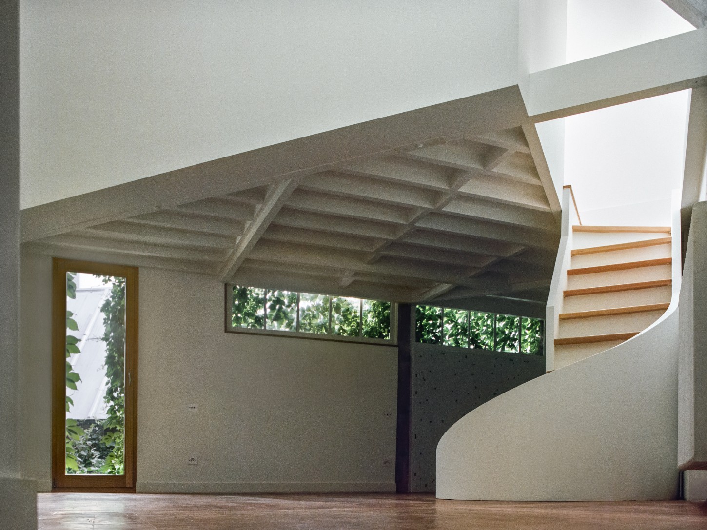 Atelier 22 by Atelier Mula Scala + Atelier Mas by Atelier Mura Scala and Atelier Mas — A double-height interior space reveals the studio's original post-and-beam timber structure overhead, with pale-finished beams and cross-bracing exposed...