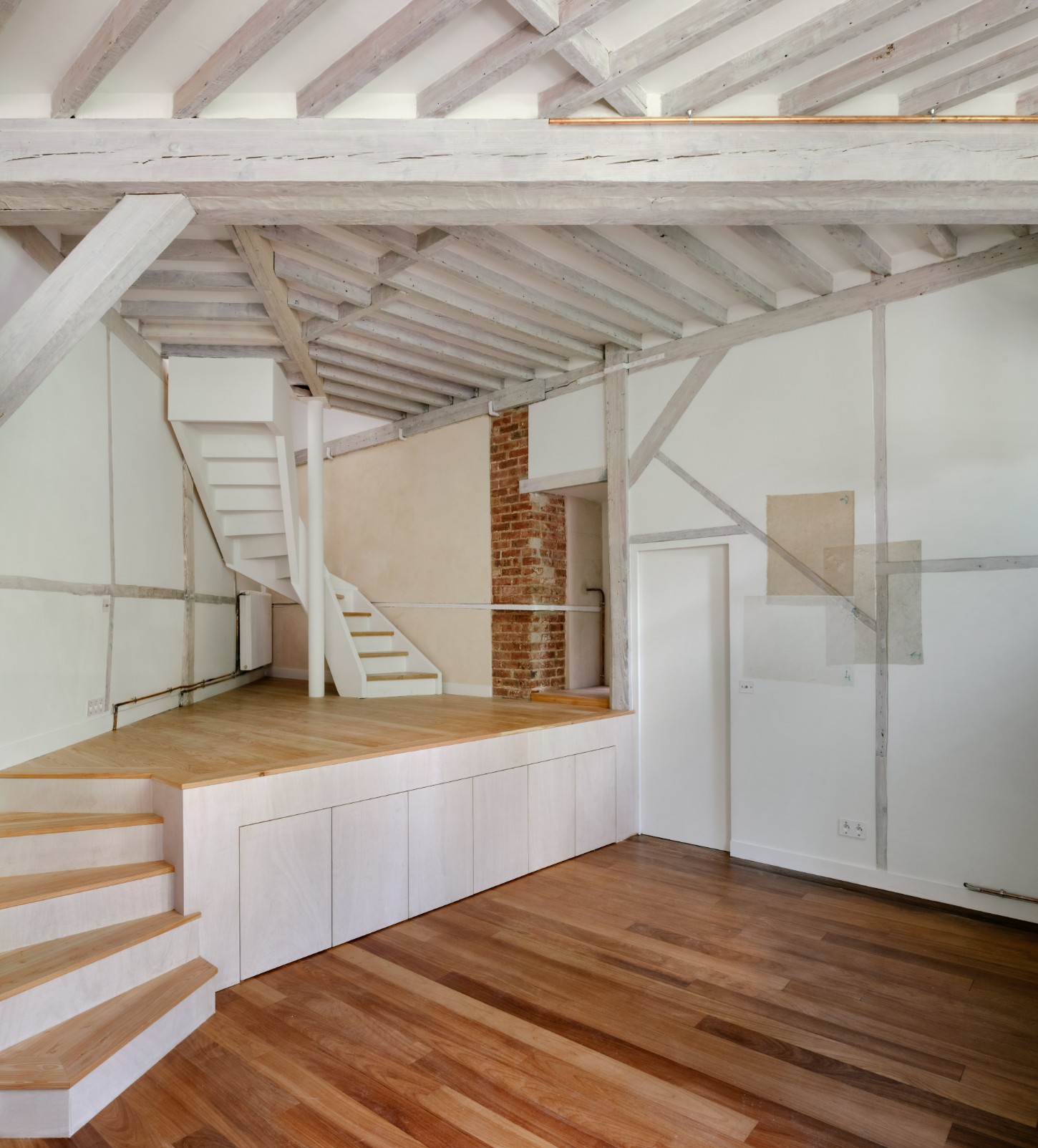 Atelier 22 by Atelier Mula Scala + Atelier Mas by Atelier Mura Scala and Atelier Mas — The renovated studio exposes its structural skeleton through pale timber beams and joists overhead, their weathered finish contrasting against white ceiling...