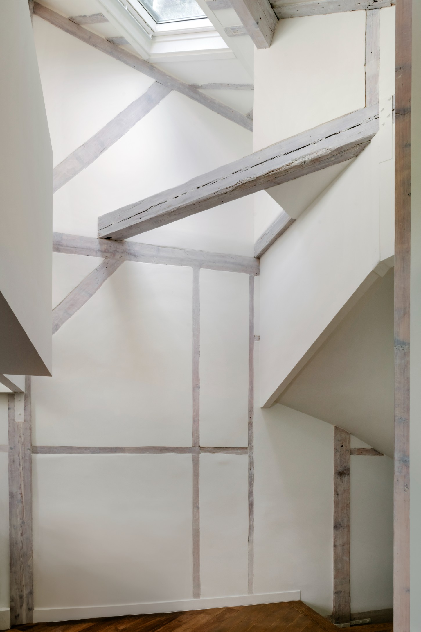 Atelier 22 by Atelier Mula Scala + Atelier Mas by Atelier Mura Scala and Atelier Mas — A sculptural staircase dominates this vertical interior space, its curved white plaster form wrapping against exposed timber beams with a pale, weathered...