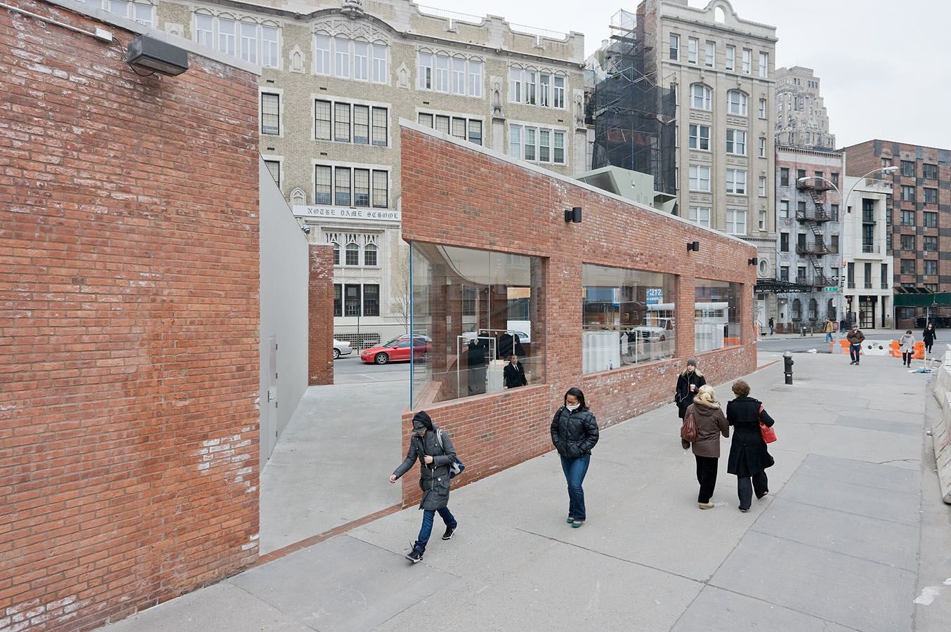 Yohji Yamamoto NYC Store by Junya Ishigami — Pedestrians navigate the carved passage bisecting Ishigami's Yamamoto store, with weathered brick walls tapering inward to frame the public throughway.