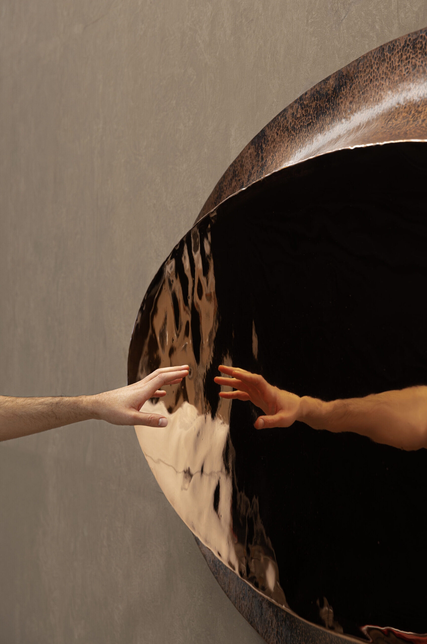 New Works by Manu Bañó — Two hands meet at the vertical seam of a fire-tempered copper dome, its surface divided into polished and oxidized halves.